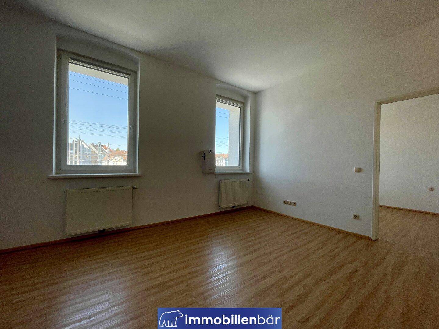Geräumiger Wohnbereich mit hellem Laminatboden und zwei großen Fenstern für viel Licht.