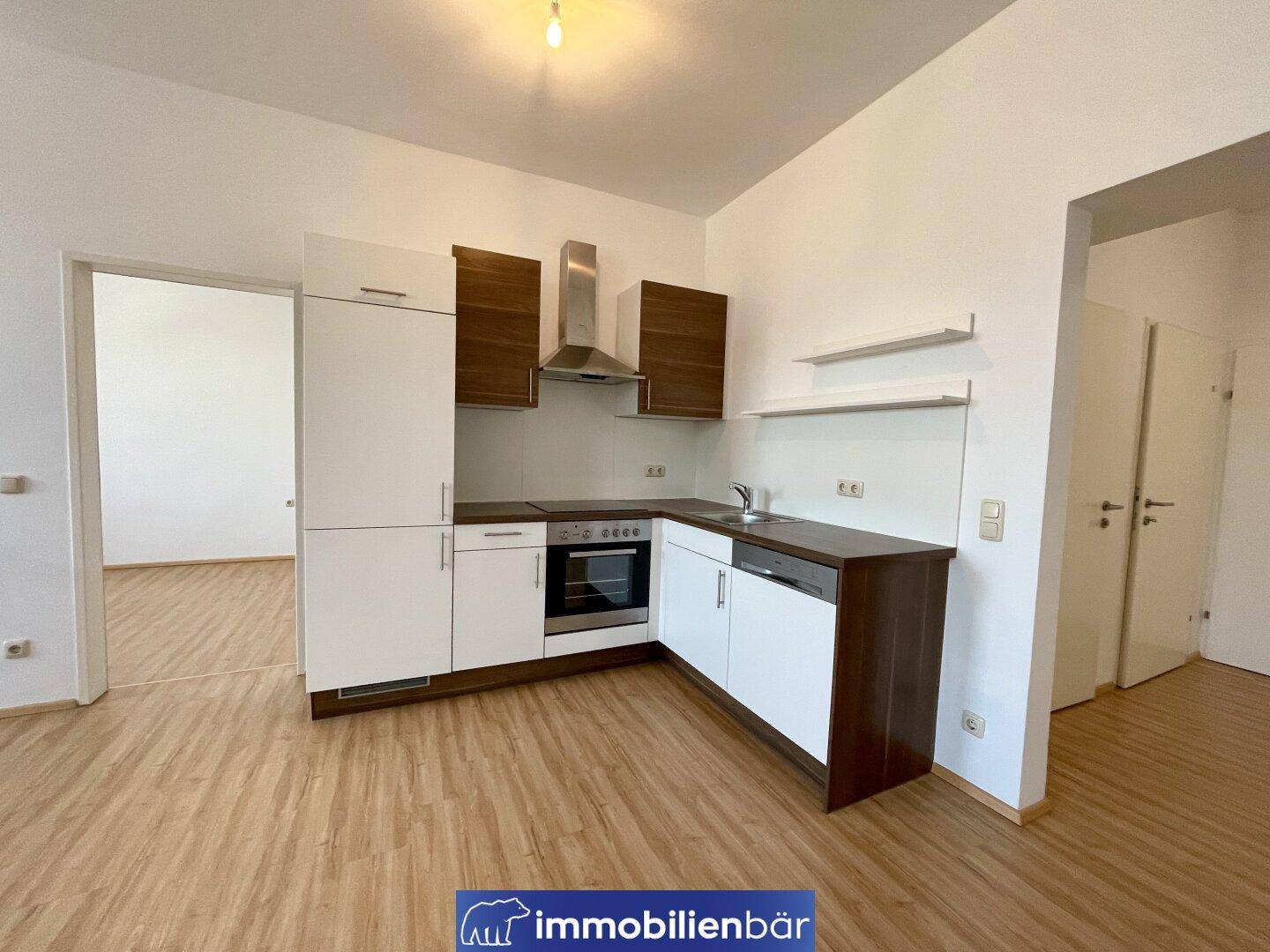Moderne Küchenzeile mit weißen und holzfarbenen Schränken, ausgestattet mit grundlegenden Geräten.