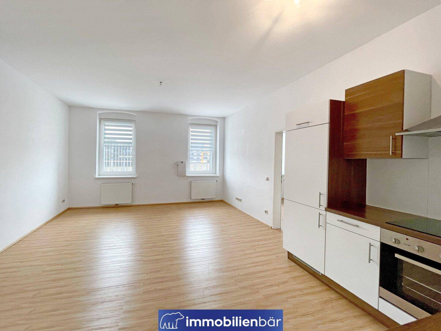 Heller Wohnbereich mit integrierter Küchenzeile und Jalousien an den Fenstern für Privatsphäre.