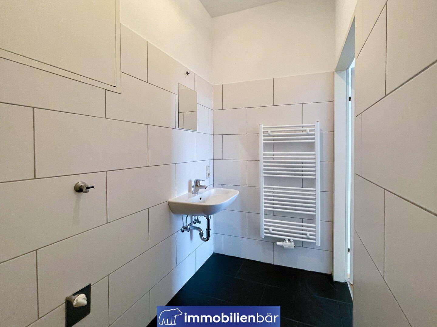 Modern gefliestes Badezimmer mit Waschbecken und beheiztem Handtuchhalter.