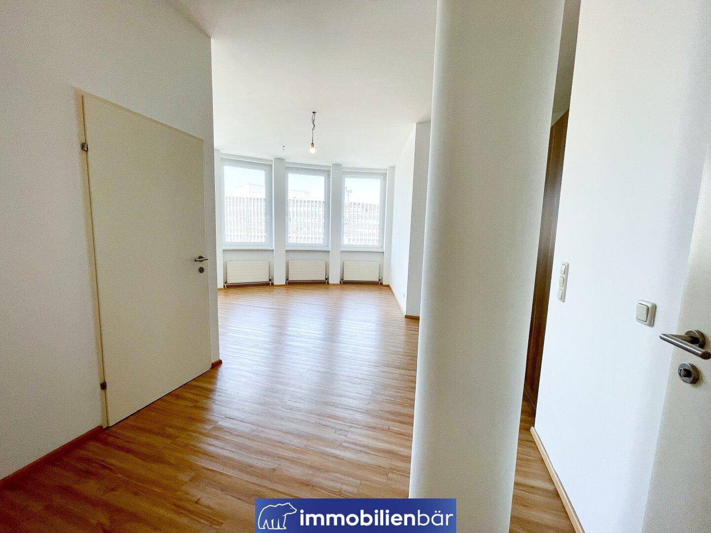 Heller Flur mit Laminatboden, der in den offenen Wohnbereich mit großen Fenstern führt.