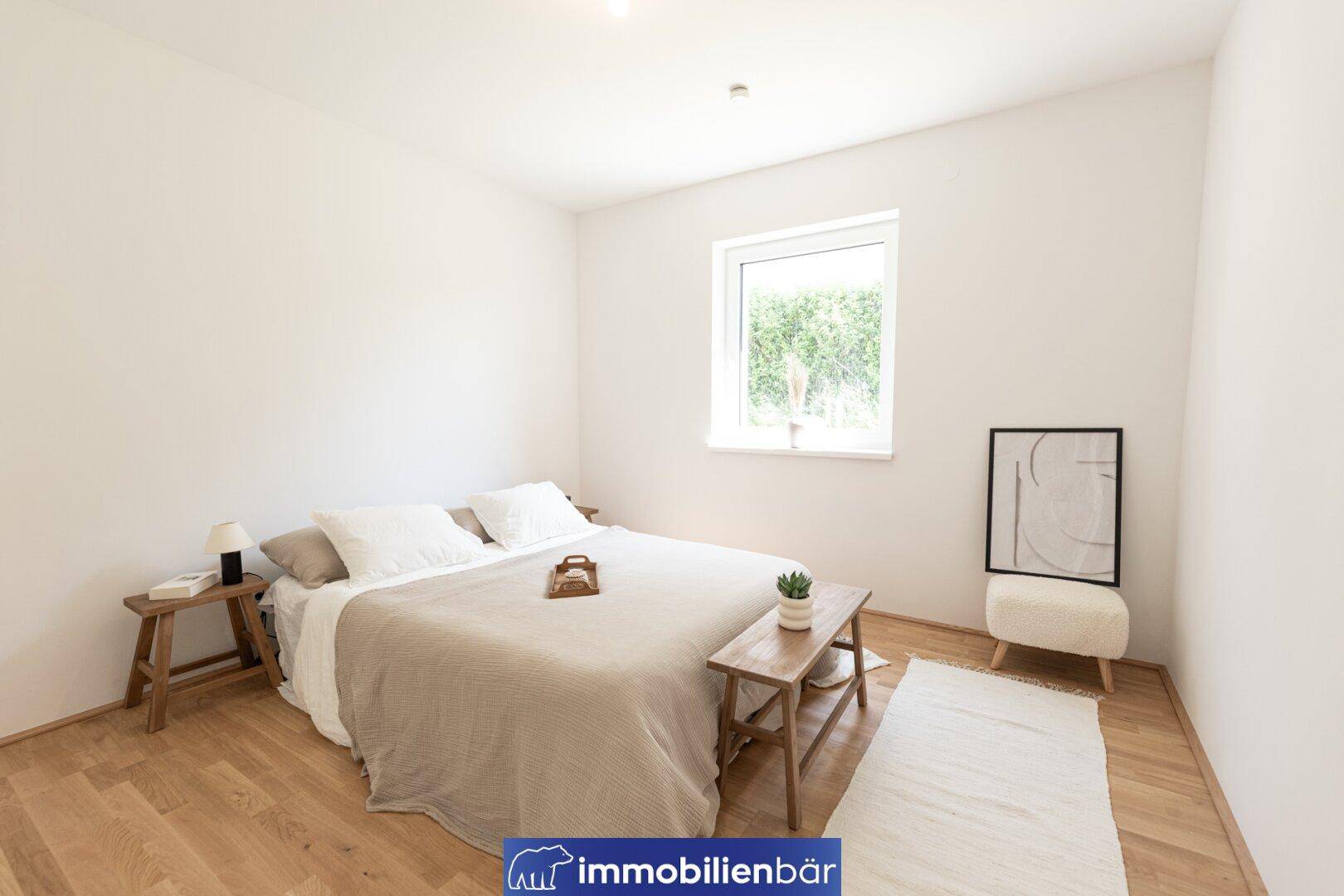 Ruhiges Schlafzimmer mit Holzboden, großem Fenster und Blick ins Grüne.