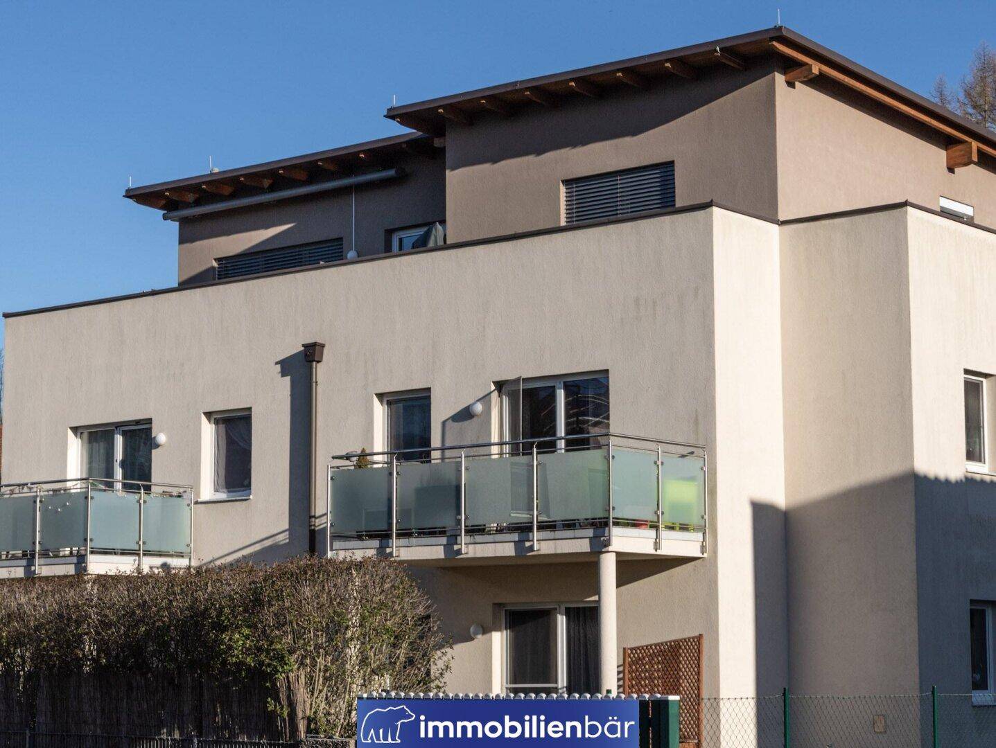 Fassade eines modernen Mehrfamilienhauses mit mehreren Balkonen und Glasgeländern unter blauem Himmel.