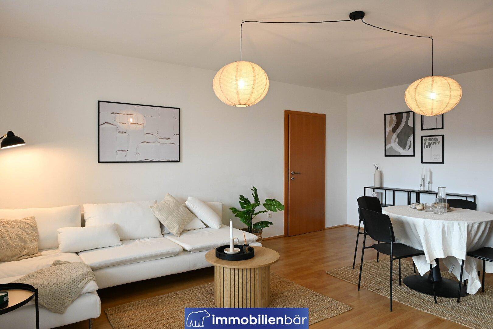 Heller Wohn- und Essbereich mit weißem Sofa, Holzboden und modernen Pendelleuchten.