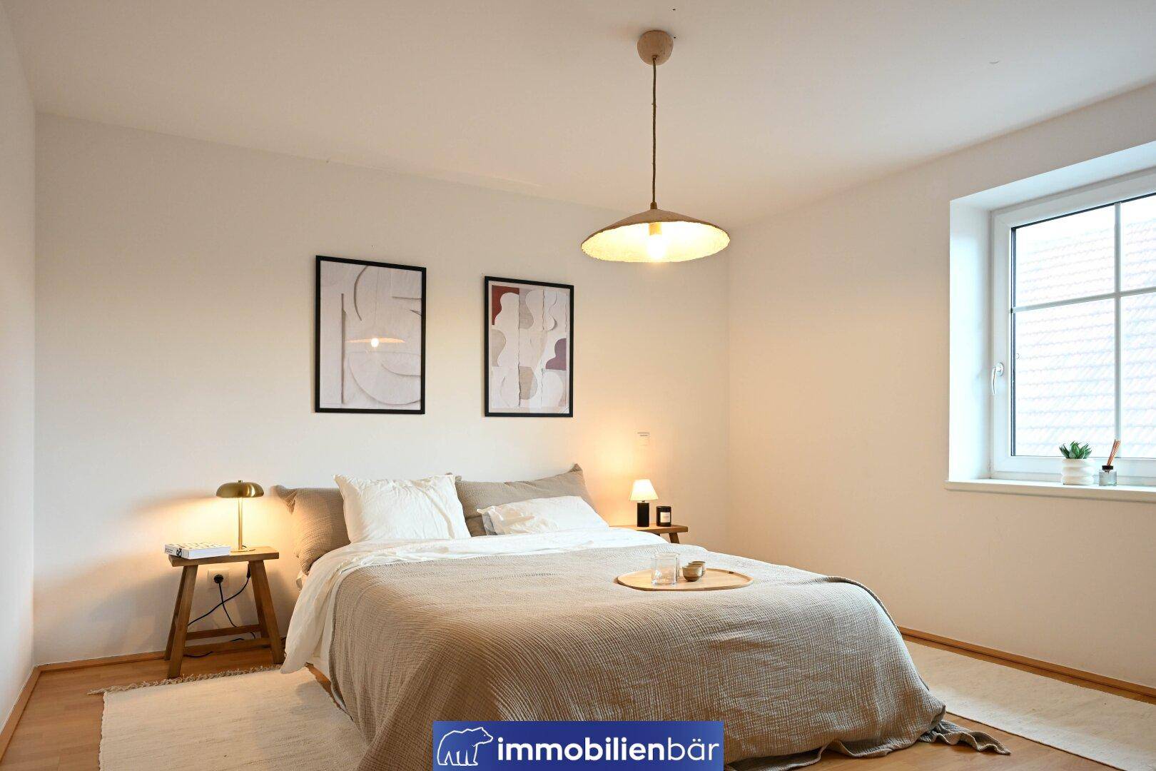 Helles Schlafzimmer mit Doppelbett, Holzboden und einem Fenster für natürliches Licht.