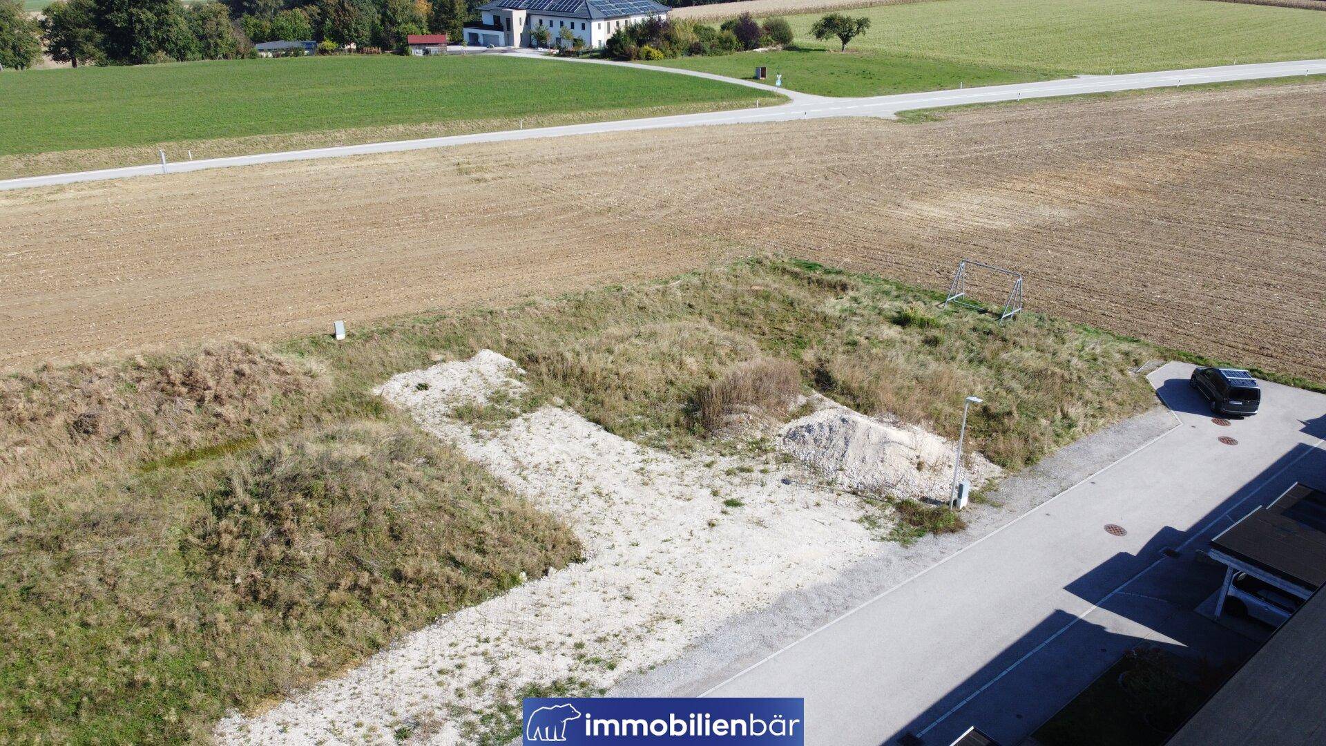 Übersicht aus der Vogelperspektive eines Baugrundstücks neben einer Straße und landwirtschaftlichen Flächen.
