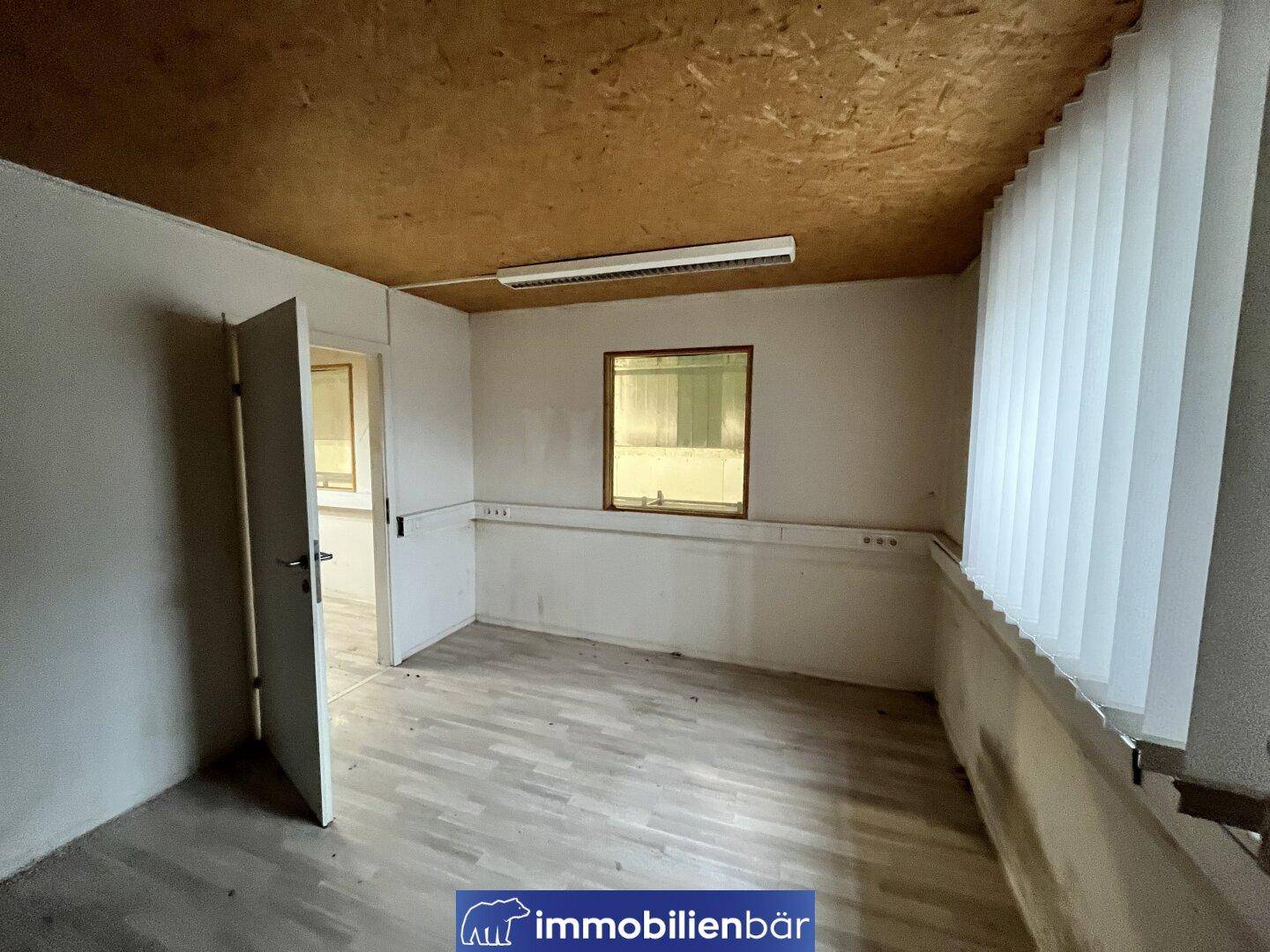 Helles Büro mit Laminatboden, Holzdecke und Jalousien am Fenster für Privatsphäre und Lichtregulierung.