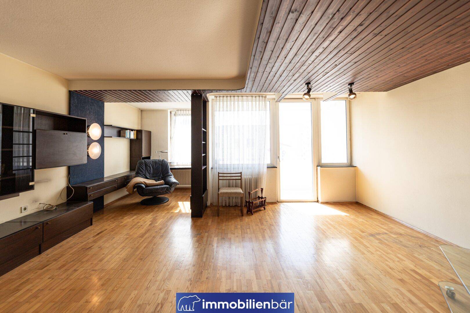 Heller Wohnbereich mit Parkettboden, Holzdecke und Zugang zu einem Balkon.