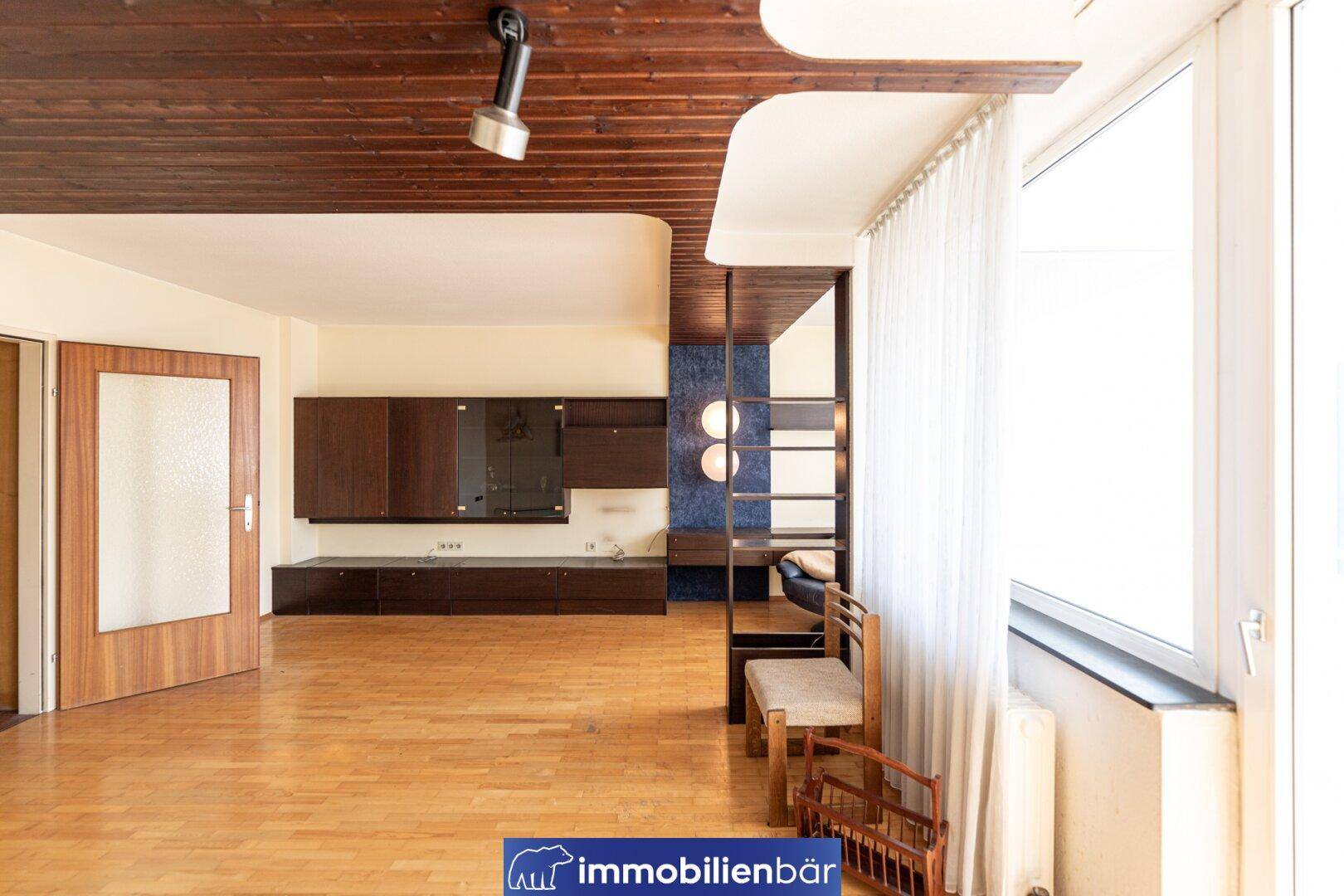 Geräumiges Wohnzimmer mit dunklen Holzmöbeln, Parkettboden und dekorativer Holzdecke.