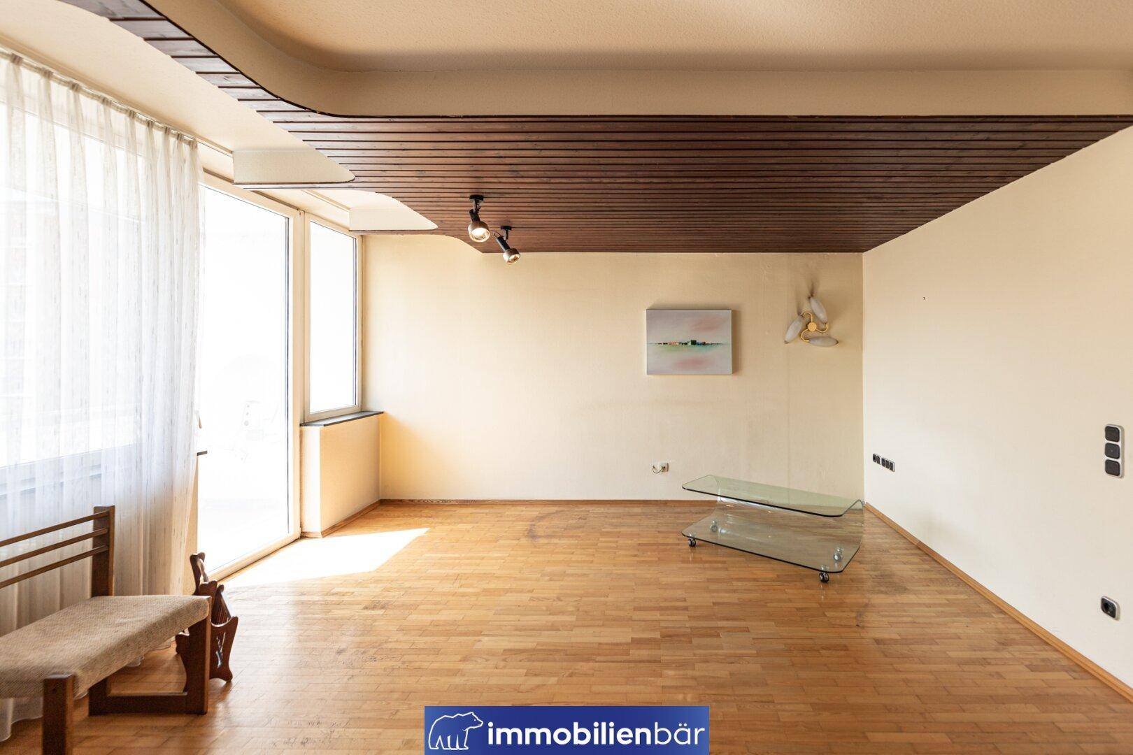 Lichtdurchfluteter Wohnraum mit Parkettboden, Holzdecke und großzügigen Fensterfronten.