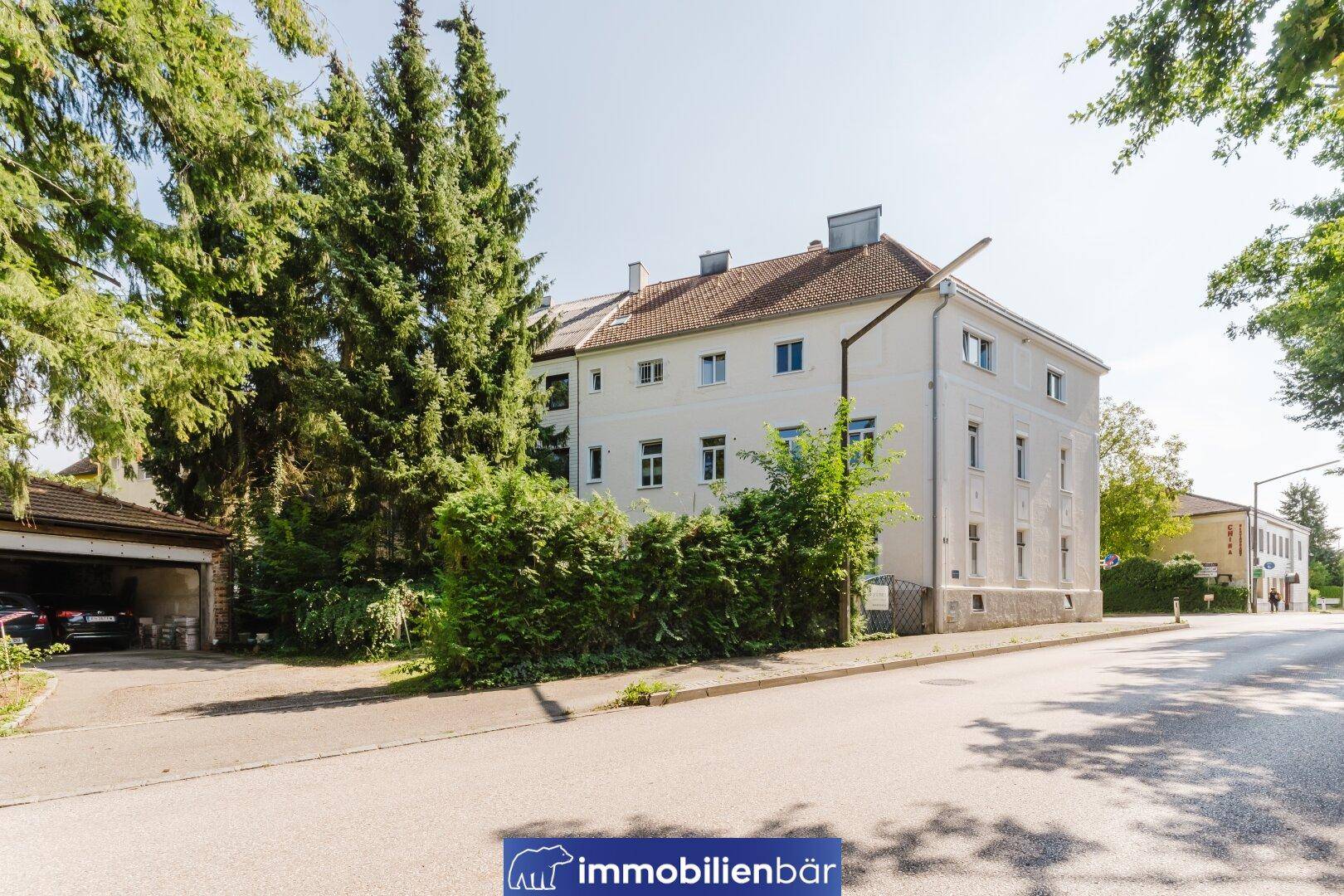 Seitenansicht des Gebäudes mit Bäumen, einer Straße und einer Garage im Vordergrund.
