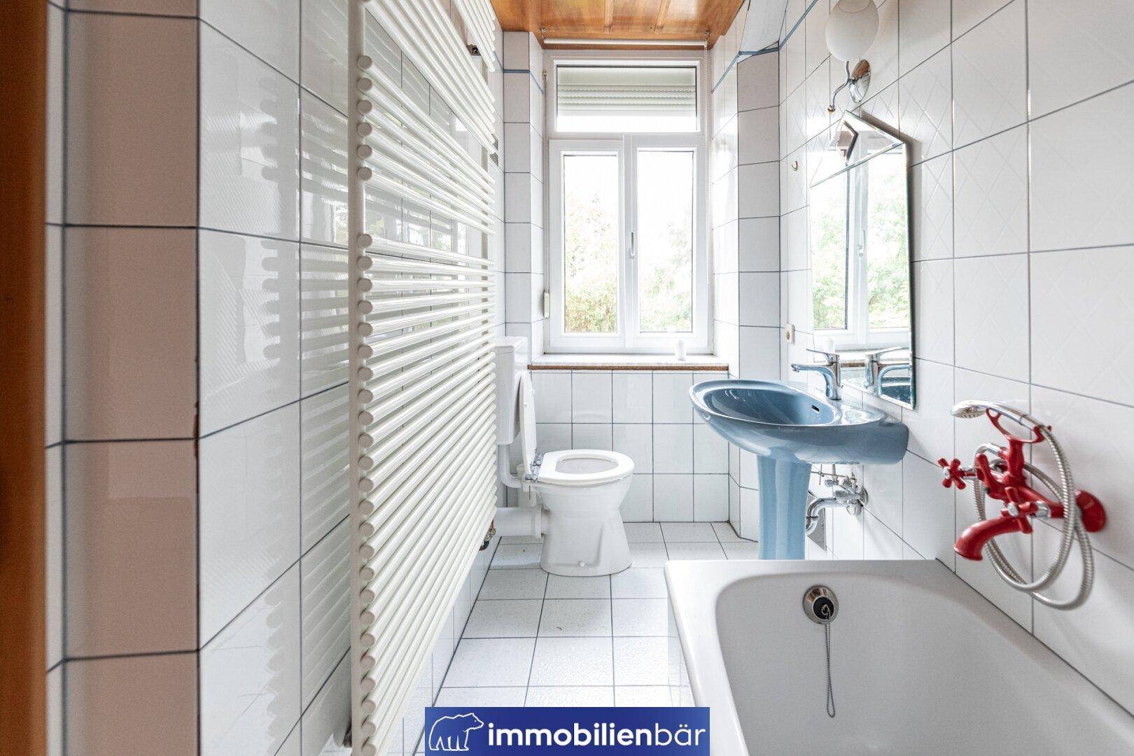 Funktionales Badezimmer mit weißen Fliesen, Badewanne, WC und beheiztem Handtuchhalter.
