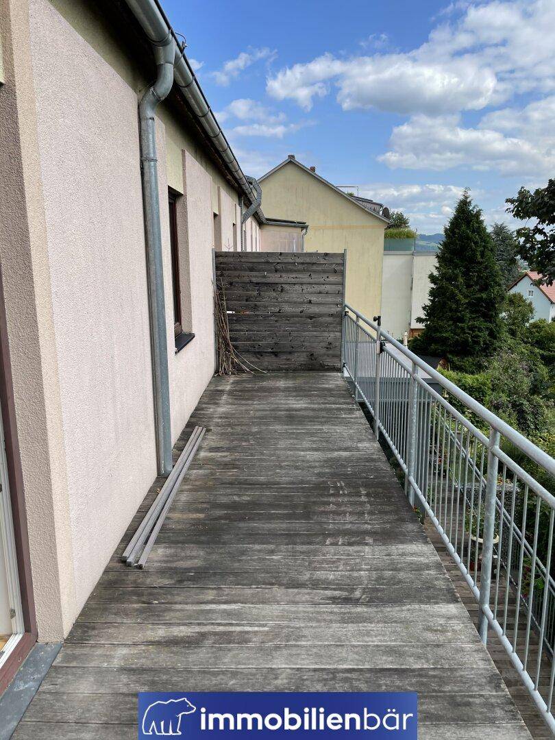 Geräumiger Holzbalkon entlang der Hausfassade mit Sichtschutz und Blick auf die Nachbarschaft.