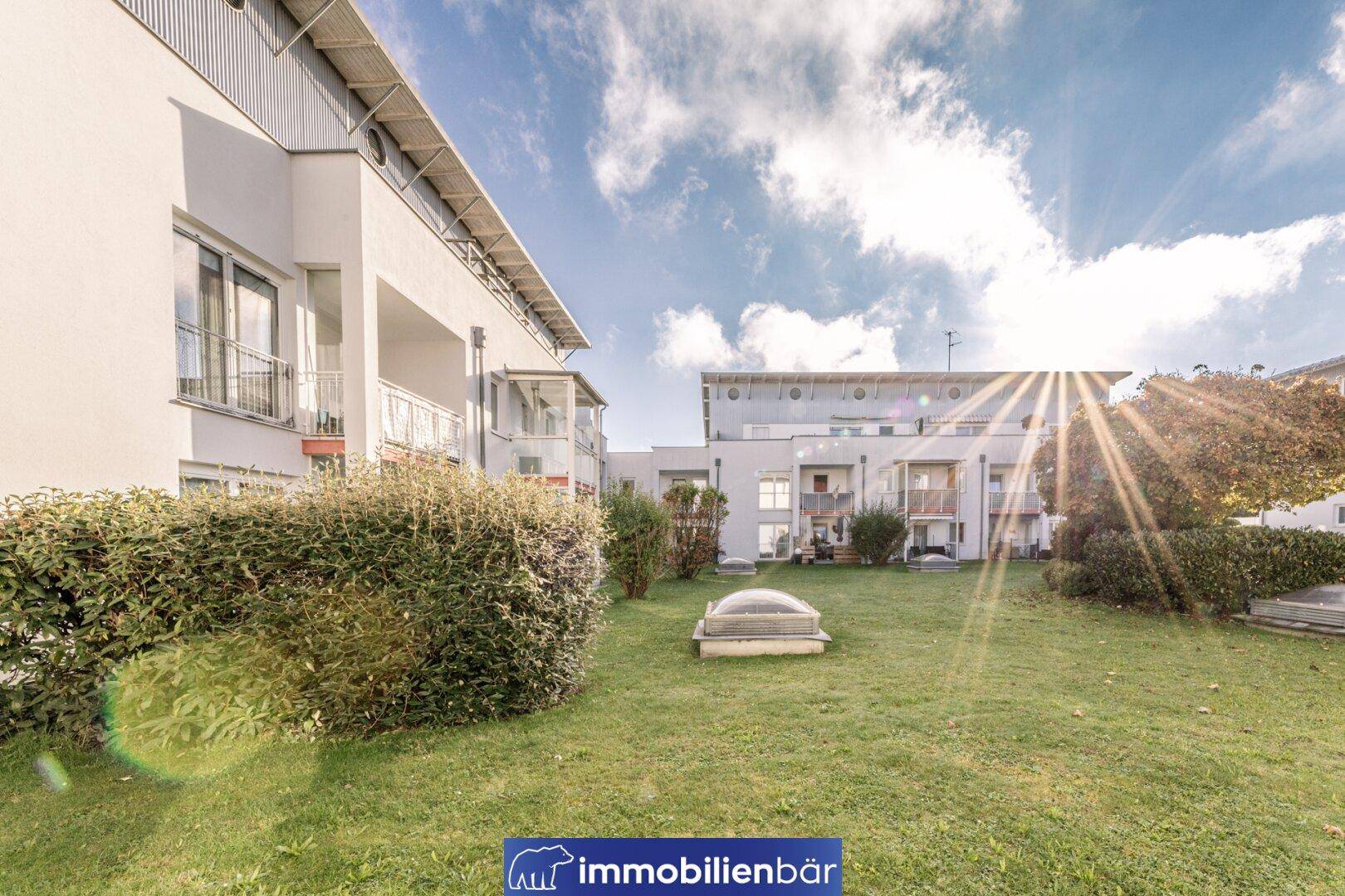 Außenansicht eines modernen Wohnkomplexes mit gepflegter Rasenfläche und Hecken unter strahlendem Himmel.