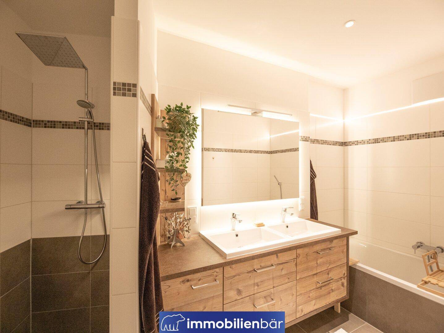 Modernes Badezimmer mit Doppelwaschbecken, großer Dusche und Badewanne im Hintergrund.