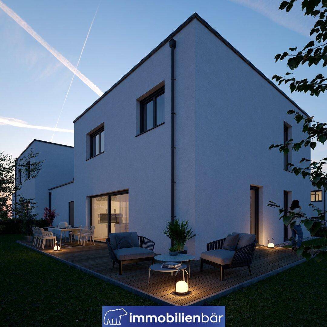 Abendliche Ansicht einer modernen Doppelhaushälfte mit beleuchteter Holzterrasse und Garten.