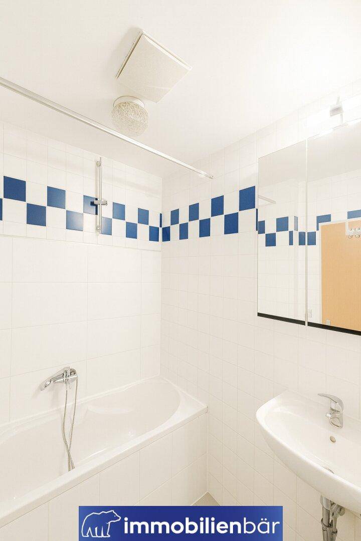 Badezimmer mit Badewanne, Waschbecken und weiß-blauen Fliesen im Schachbrettmuster.