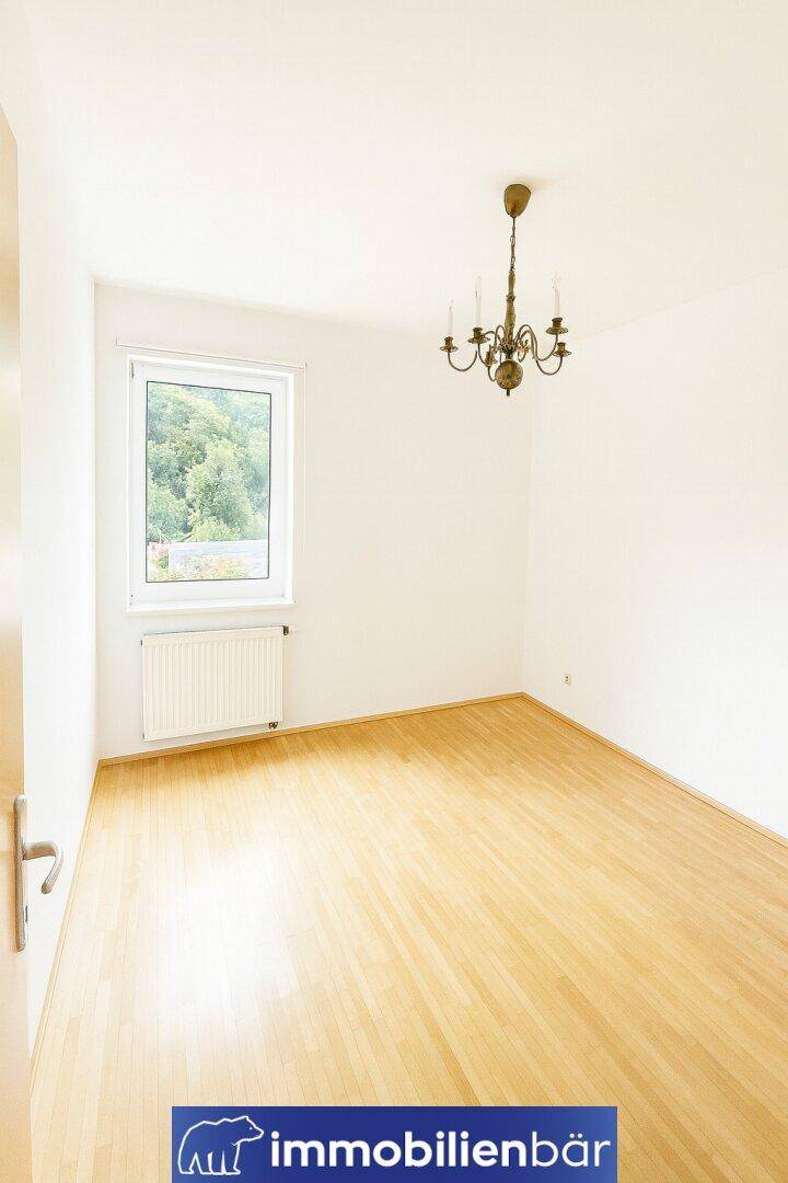 Helles Zimmer mit Laminatboden, großem Fenster und klassischem Kronleuchter.