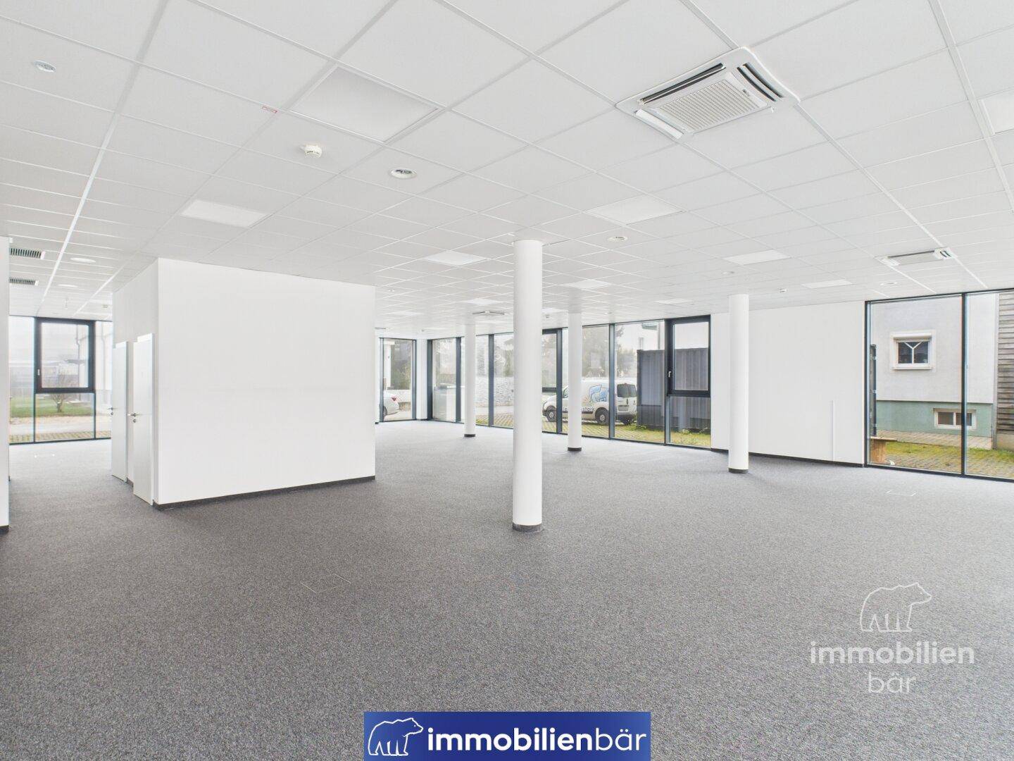 Heller, offener Bürobereich mit Säulen und großen Fenstern, die einen Blick nach draußen ermöglichen und eine angenehme Arbeitsatmosphäre bieten.