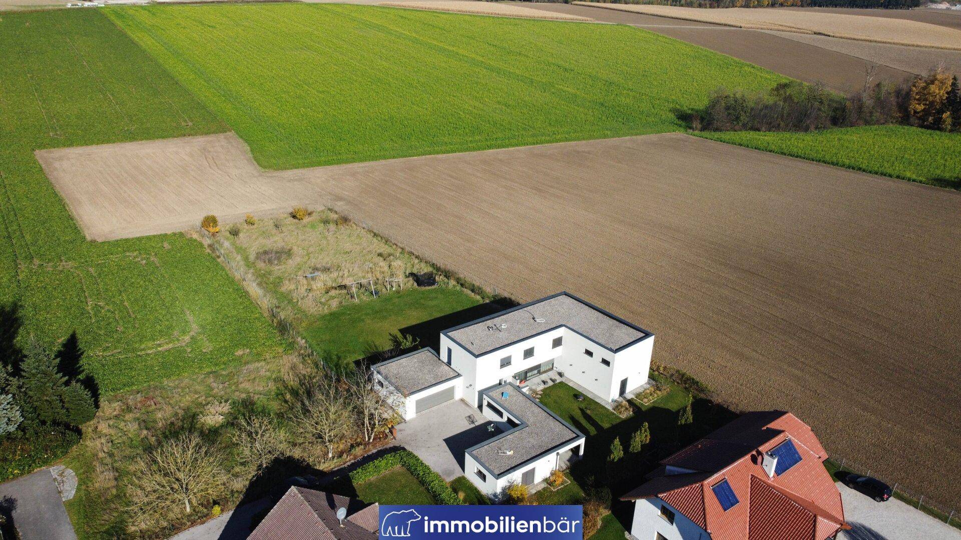 Luftaufnahme des modernen Wohnhauses mit umliegenden Feldern und Grünflächen.