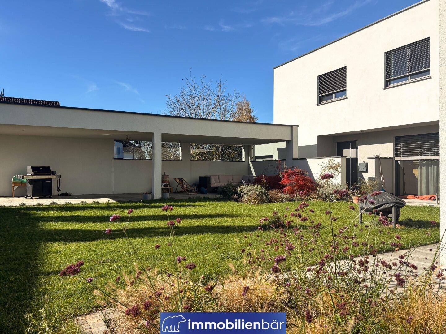 Weitläufiger Garten mit Rasenfläche und moderner Architektur des Hauses unter blauem Himmel.