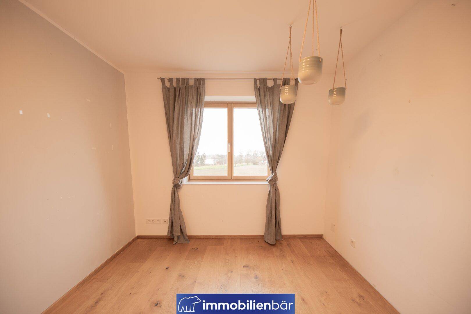 Helles Schlafzimmer mit Holzboden und Fenster, das einen ruhigen Blick ins Grüne bietet.