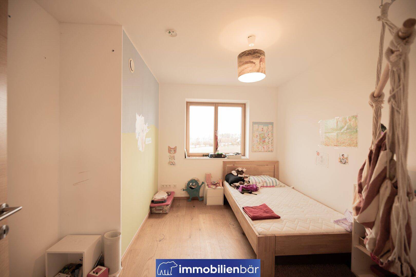 Kinderzimmer mit Holzboden, Einzelbett und farbenfroher Wandgestaltung, hell und freundlich.
