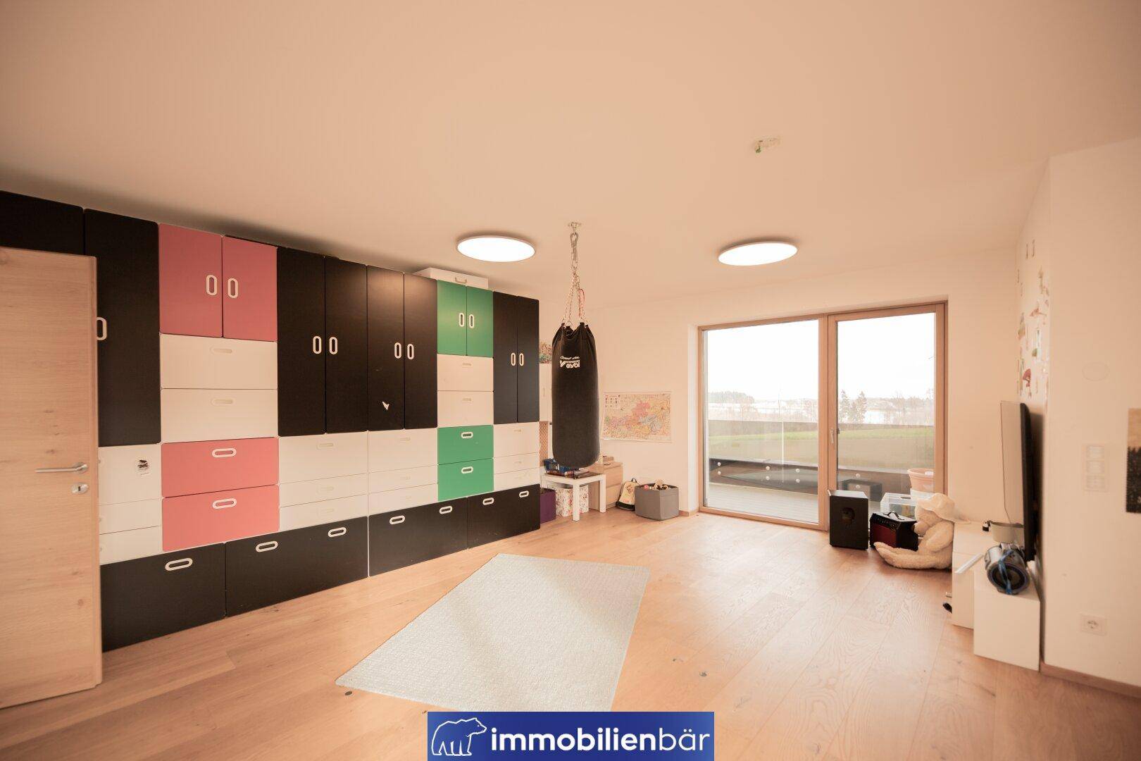 Geräumiges Zimmer mit Holzboden, bunten Schränken und einem Boxsack, ideal als Fitness- oder Spielzimmer.