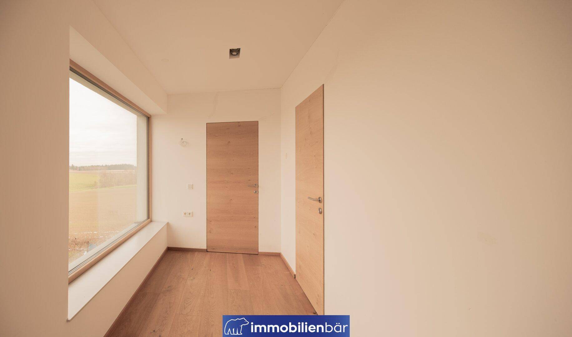 Helles Zimmer mit Holzboden und großem Fenster, das einen weiten Blick auf die Landschaft bietet.