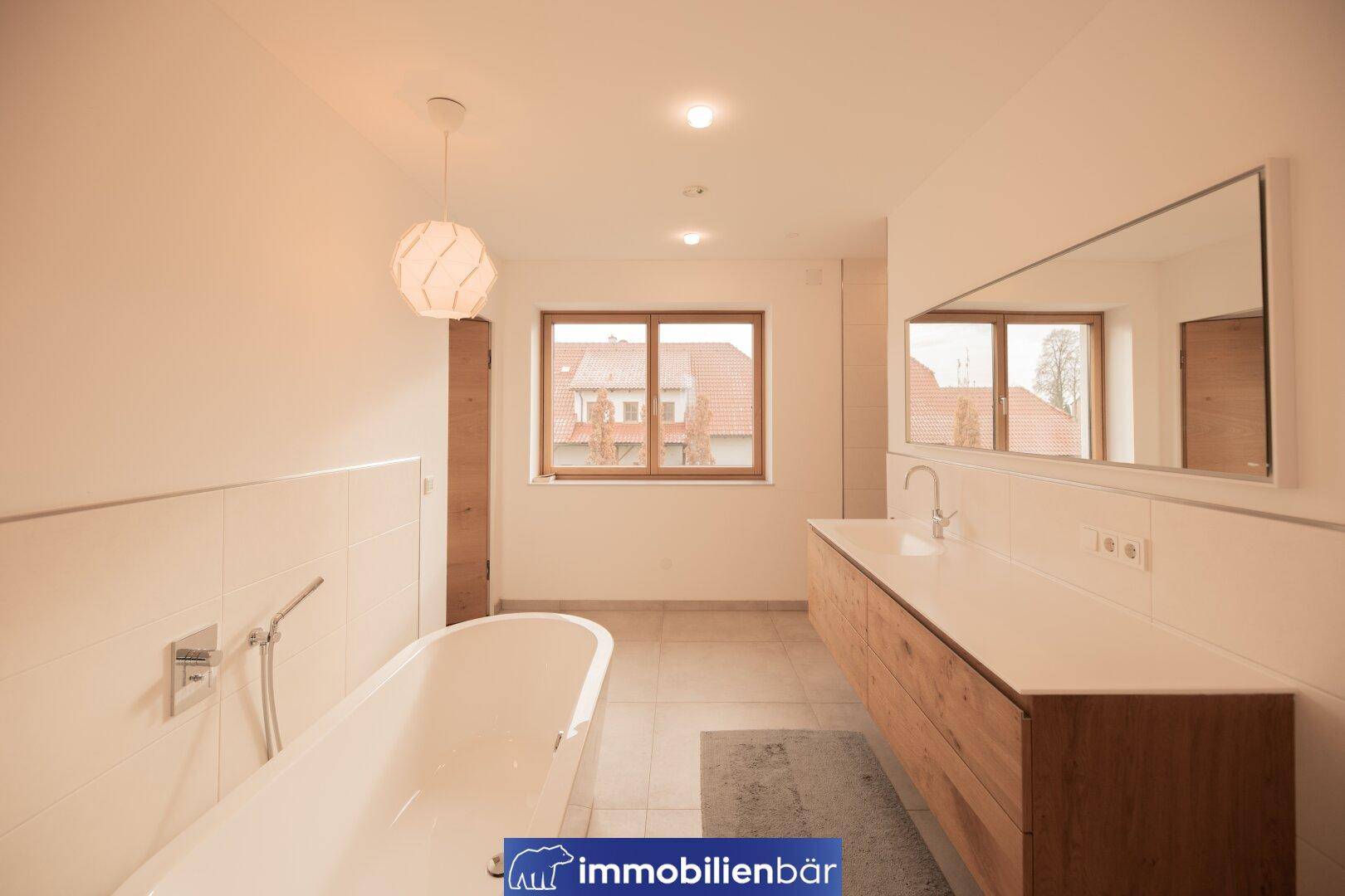 Großes Badezimmer mit freistehender Badewanne, Doppelwaschtisch und Fenster, hell und modern.