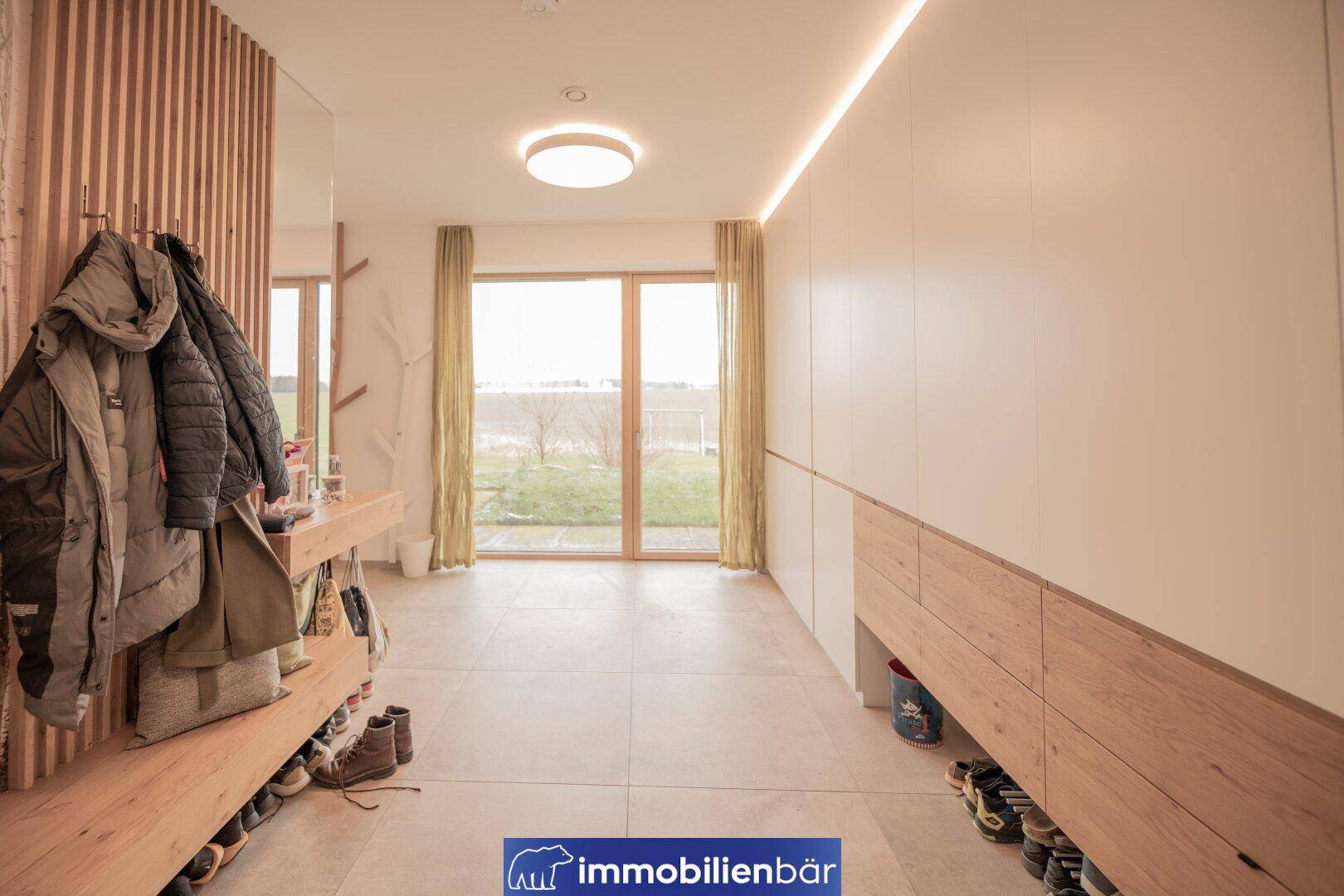 Heller Eingangsbereich mit Garderobe, Einbauschränken und großen Fenstern mit Blick ins Freie.