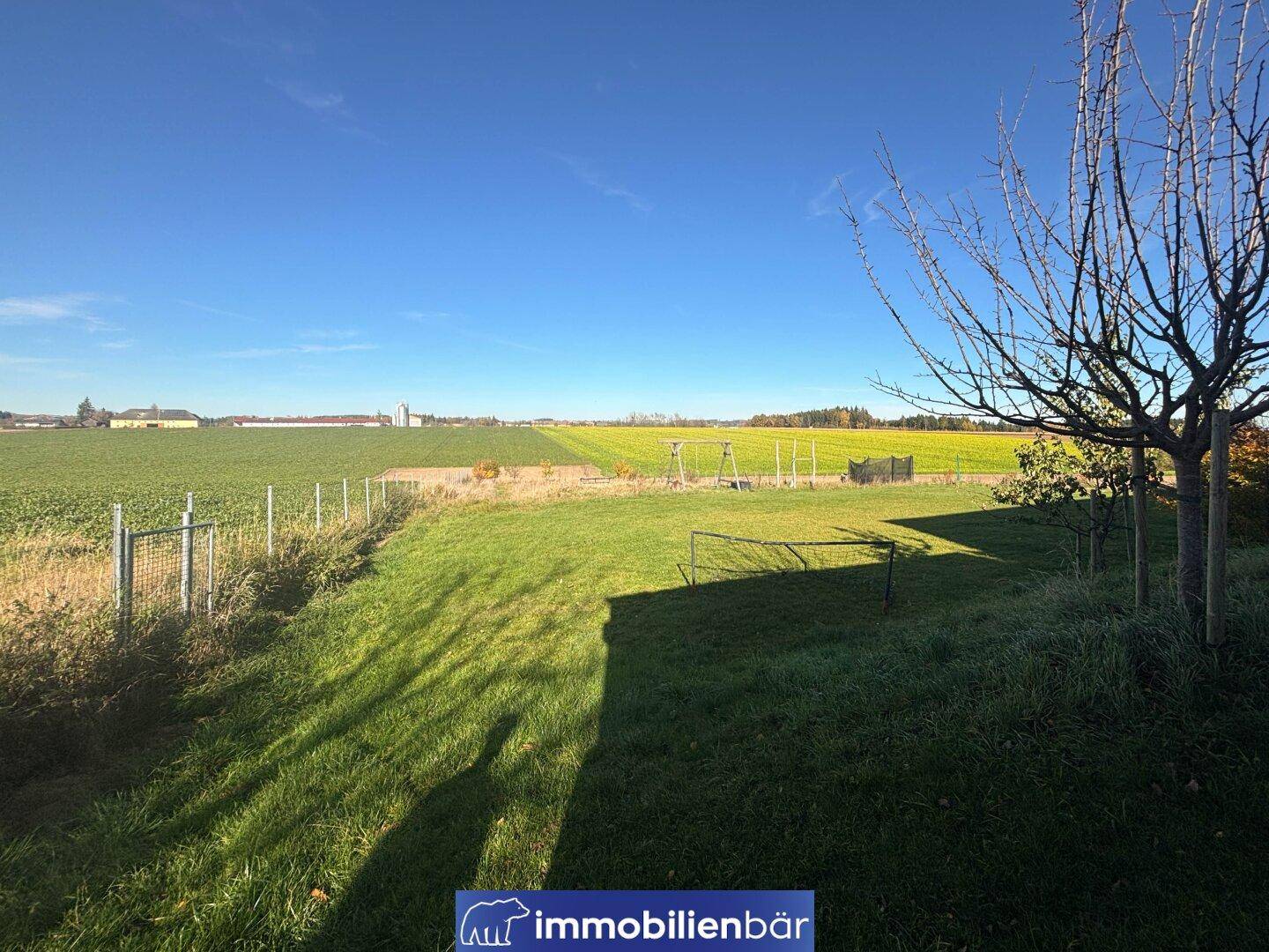 Große Rasenfläche und angrenzende Felder unter strahlend blauem Himmel, ideal für Outdoor-Aktivitäten.