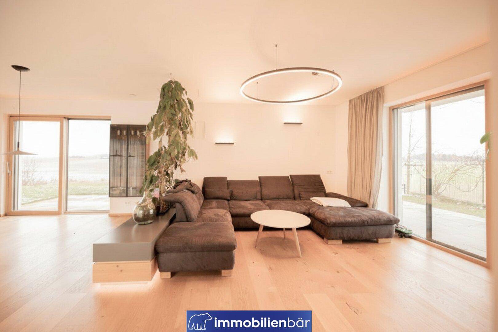 Gemütlicher Wohnbereich mit großem Ecksofa, Holzboden und Zugang zu einer Außenterrasse.