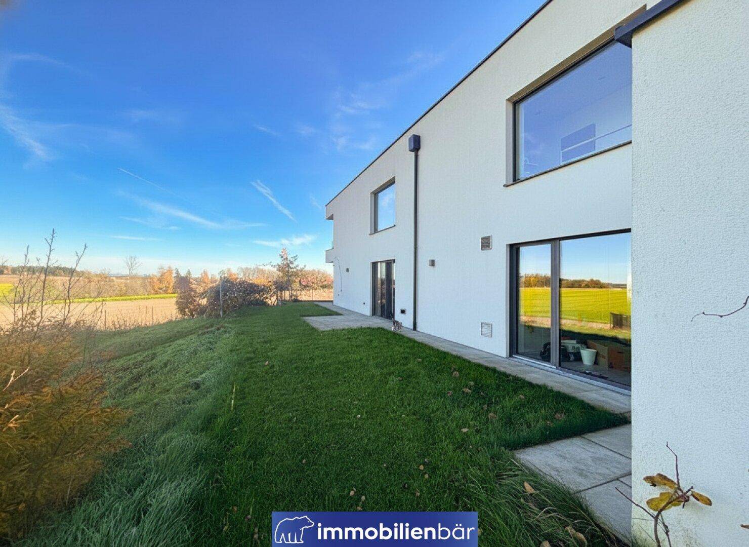 Seitenansicht des modernen Hauses mit großen Fenstern und einer gepflegten Rasenfläche.