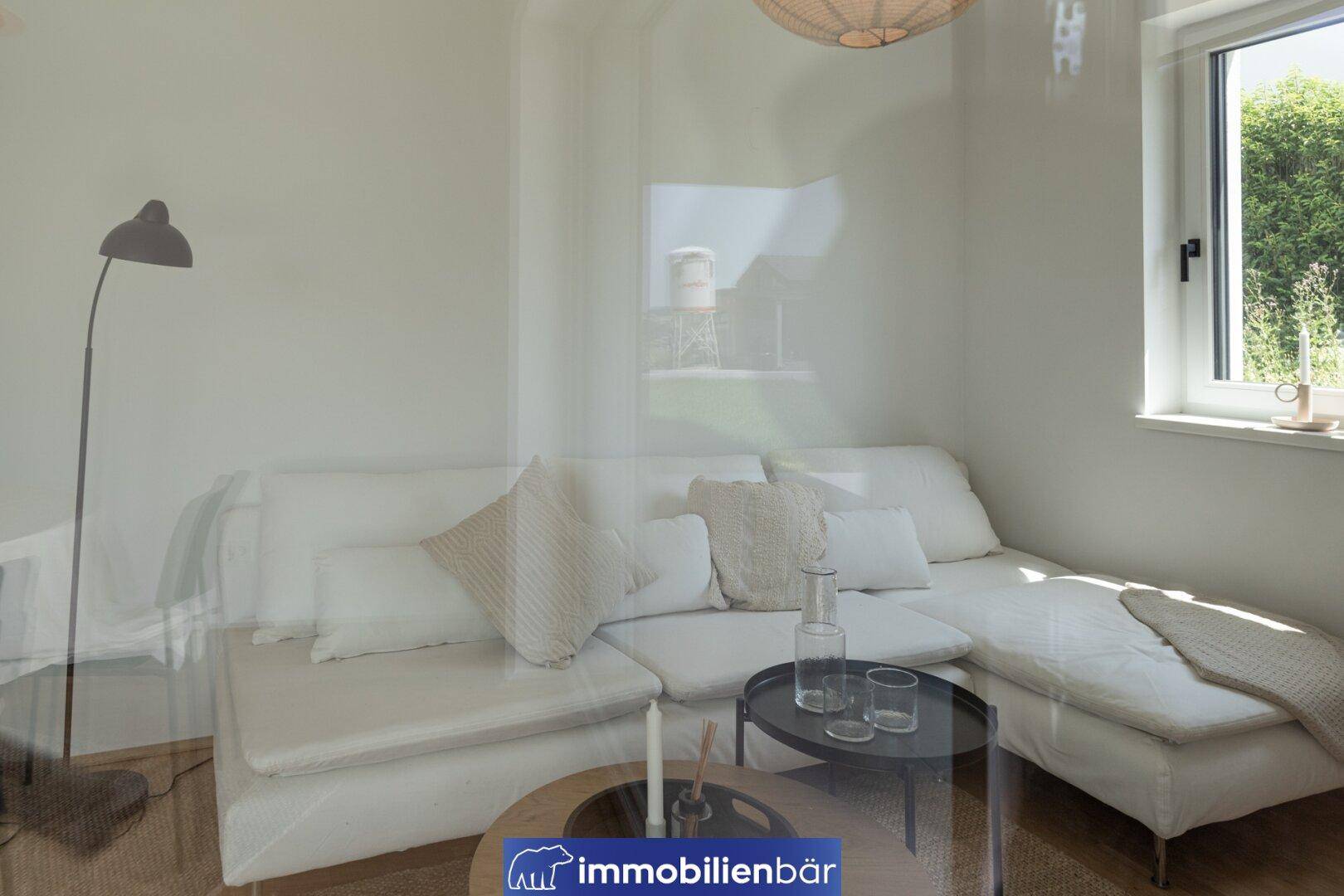 Gemütlicher Wohnbereich mit weißem Sofa, Stehlampe und Fenster, das viel Tageslicht hereinlässt.