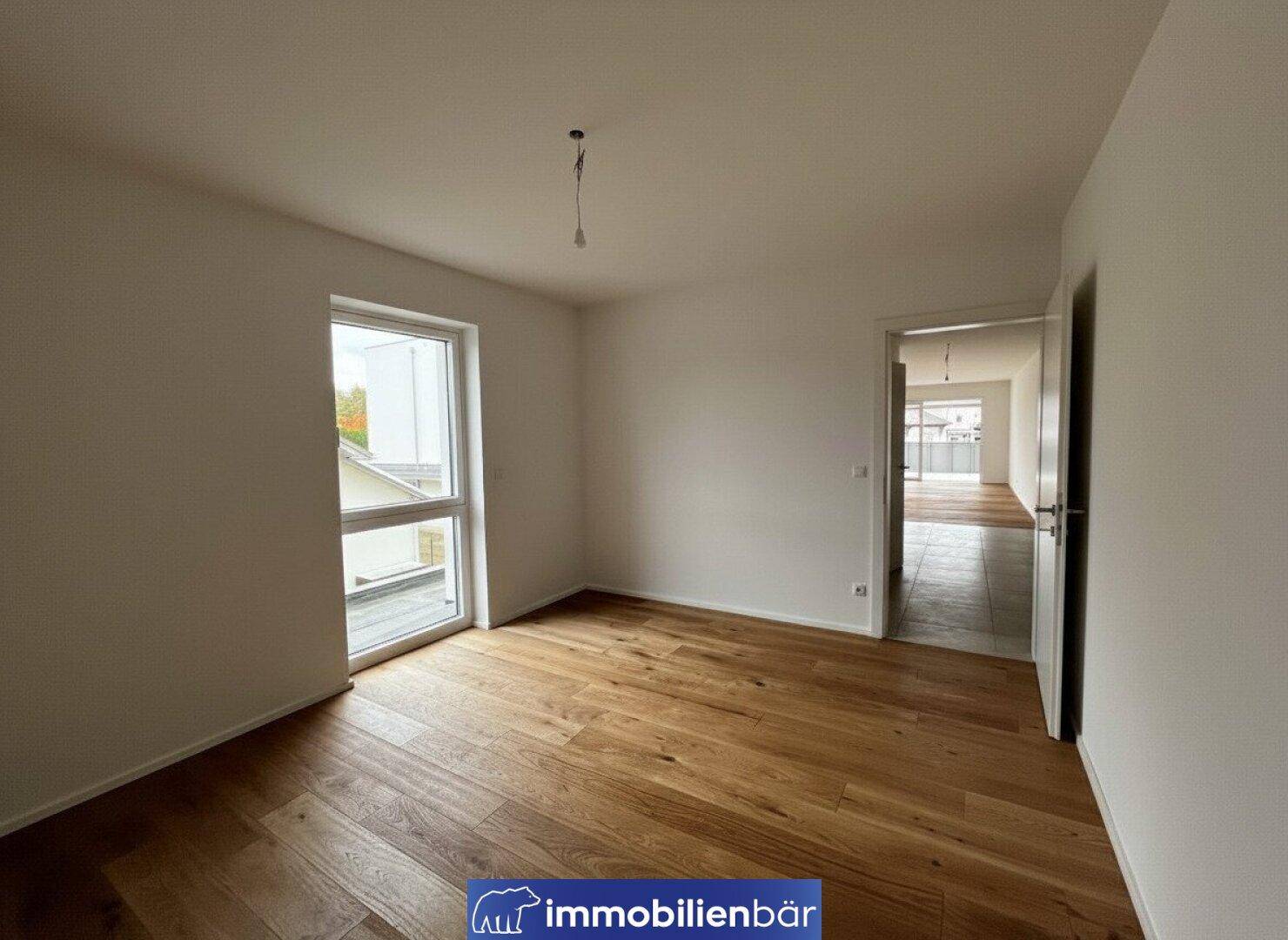 Helles Schlafzimmer mit Holzboden und großem Fenster, das einen Blick nach draußen bietet.