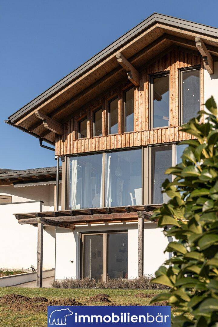 Moderne Architektur mit Holzfassade und großen Fensterfronten, umgeben von Grün.