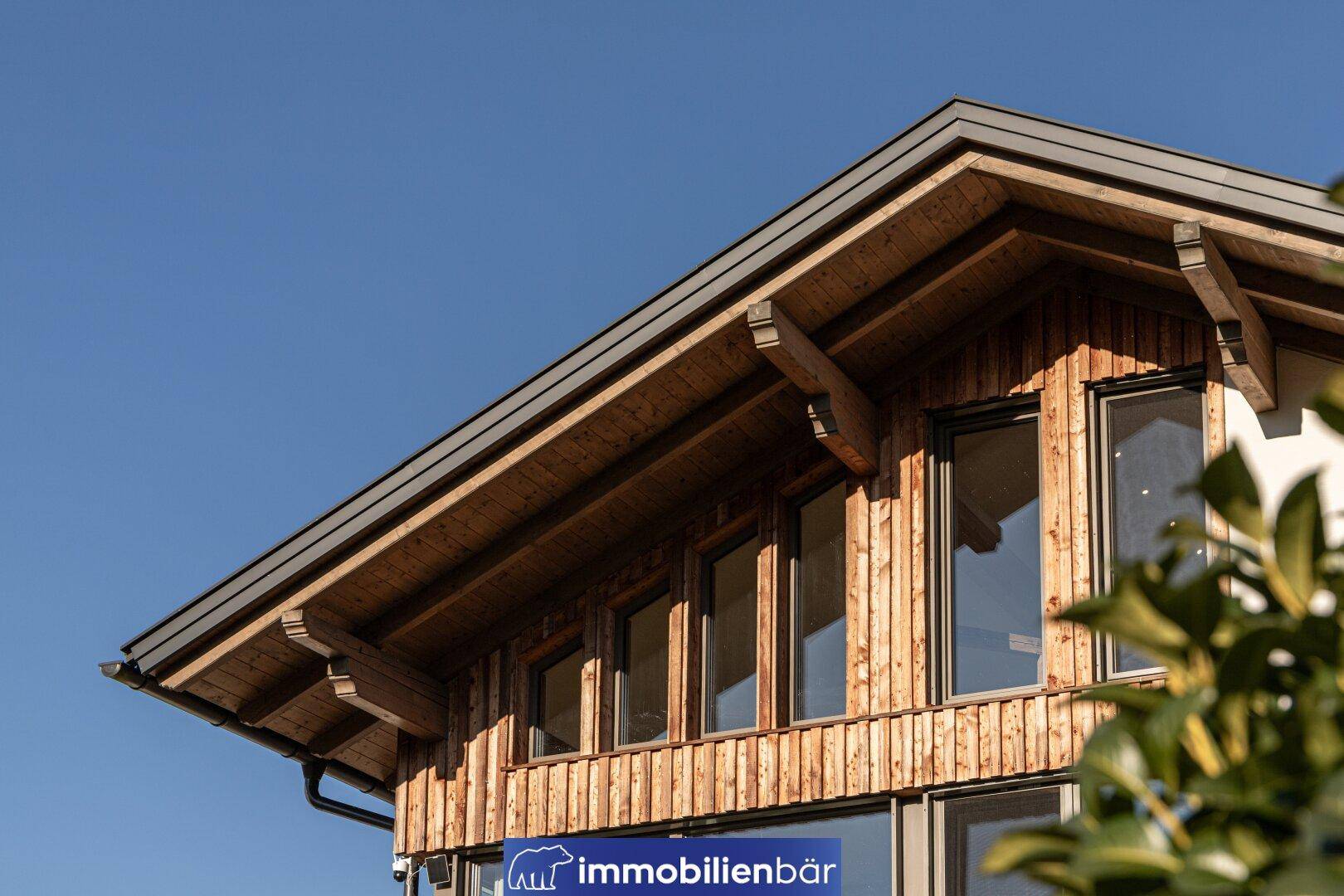 Detailansicht der modernen Holzfassade mit Dachüberstand und großen Fenstern.