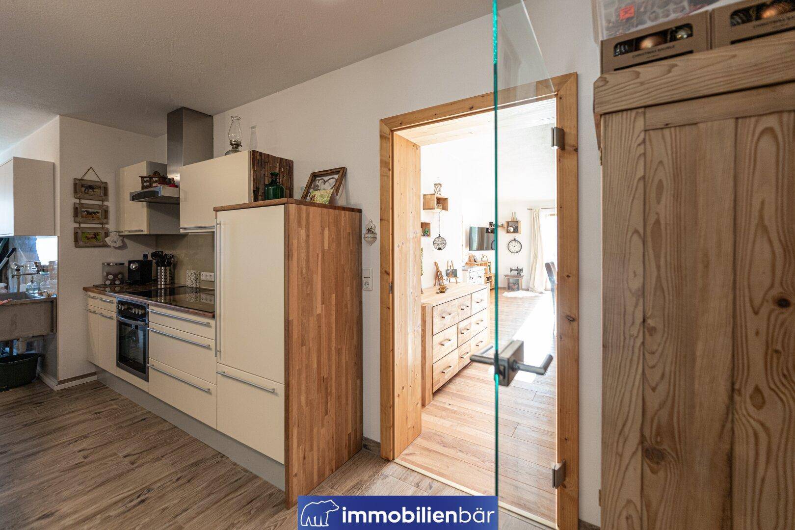 Moderne Küche mit hellen Fronten, Holzelementen und Blick in den Wohnbereich.