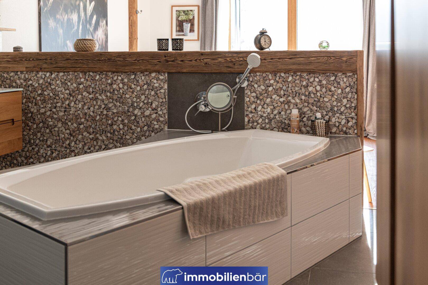 Elegante Badewanne in einem modernen Badezimmer mit Steinakzenten und Fliesenboden.