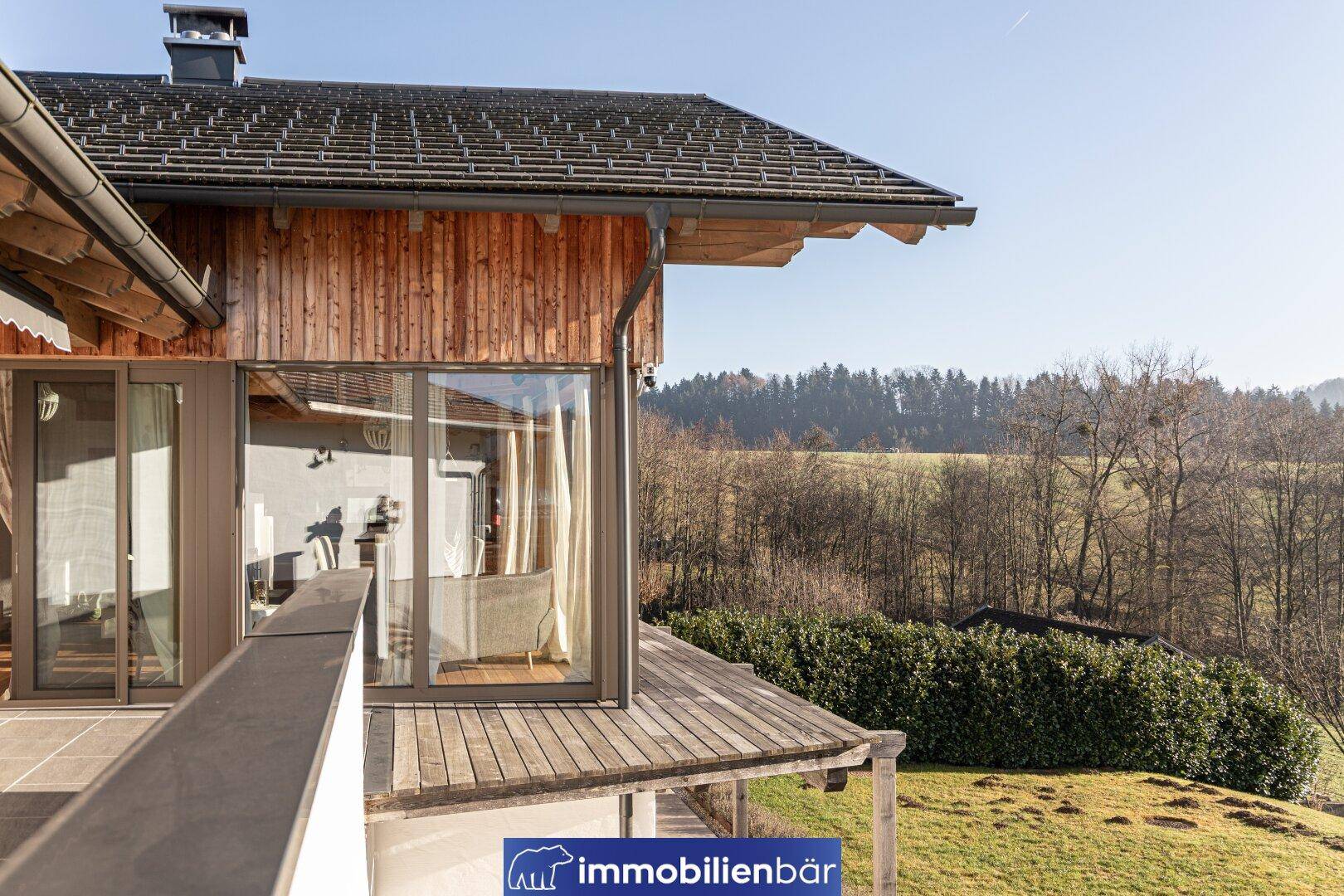 Balkon mit Holzboden und weitem Blick über die grüne Landschaft und Bäume.