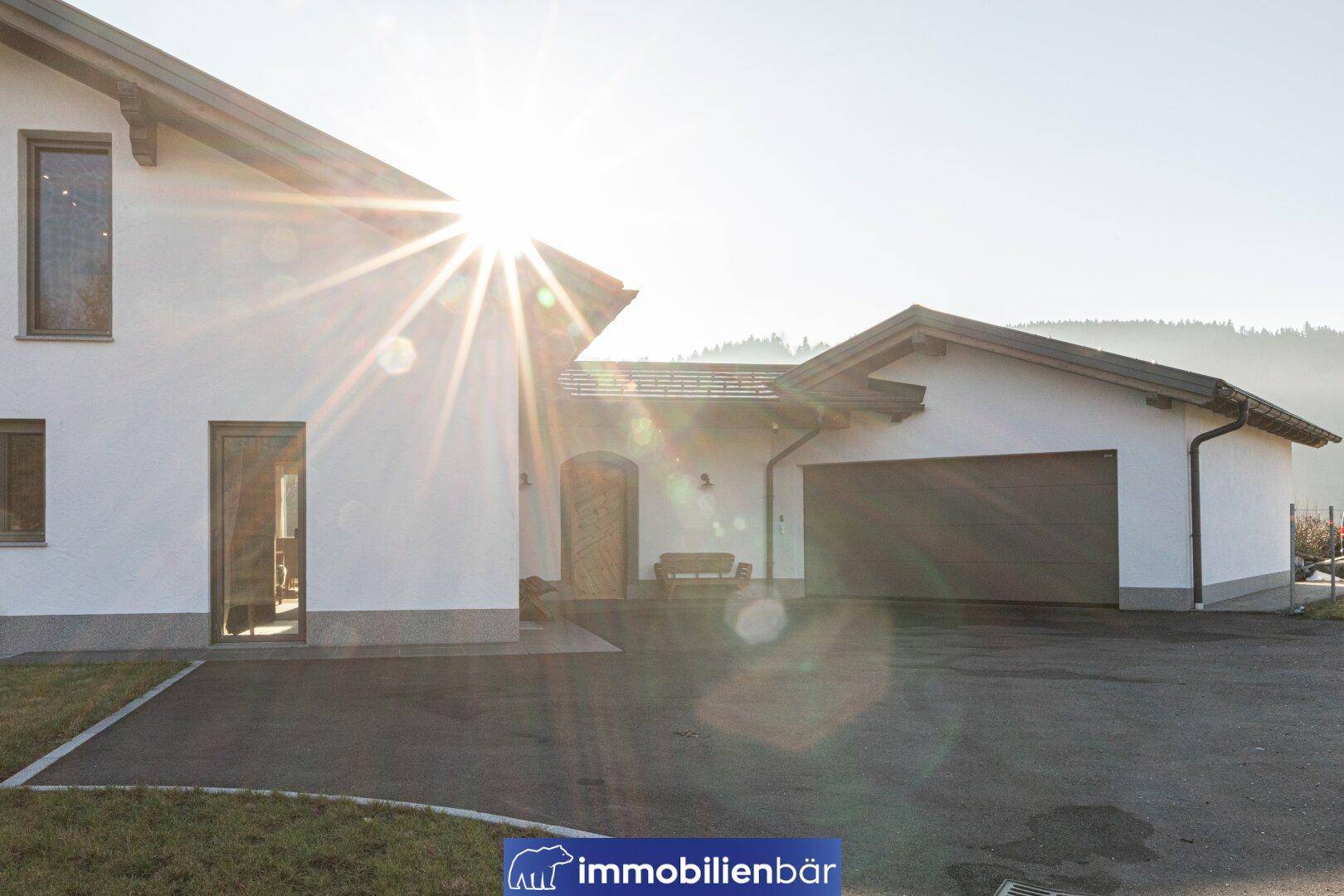Modernes Einfamilienhaus mit Garage und weitläufiger Auffahrt unter strahlendem Sonnenschein.