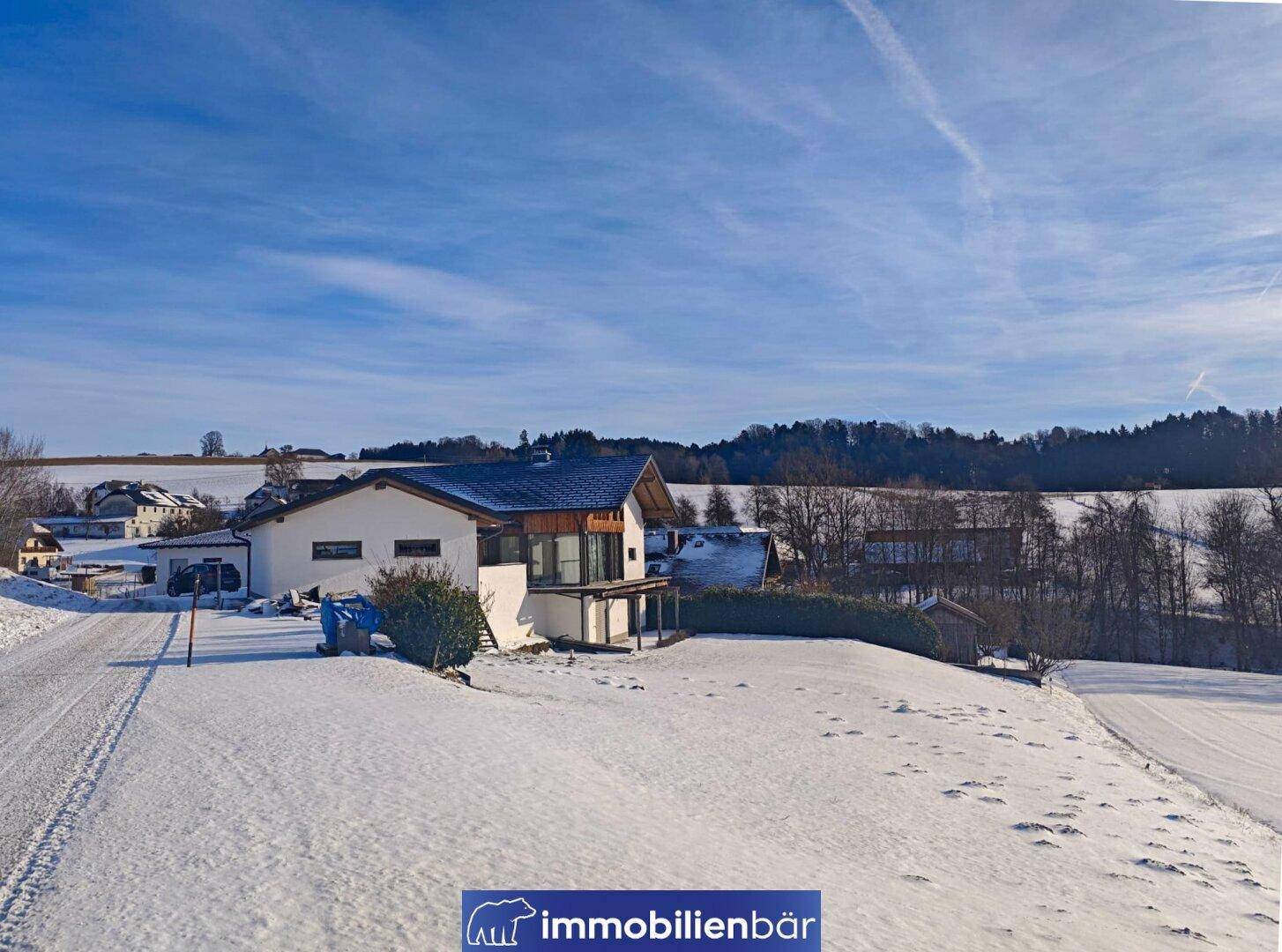 Winterlandschaft mit Einfamilienhaus, umgeben von verschneiten Feldern und Bäumen.