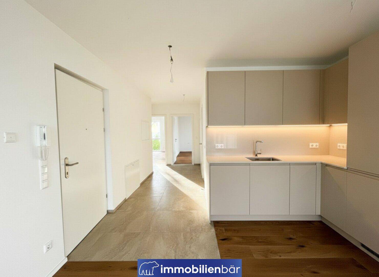 Offener Eingangsbereich mit integrierter Küchenzeile in Beige und Fliesenboden, bereit zur Einrichtung.