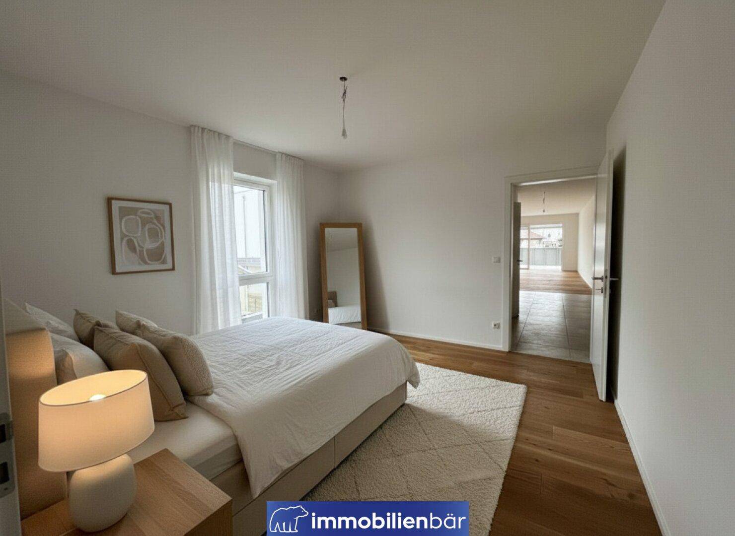 Gemütliches Schlafzimmer mit Holzboden, großem Bett und Fenster mit hellen Vorhängen.