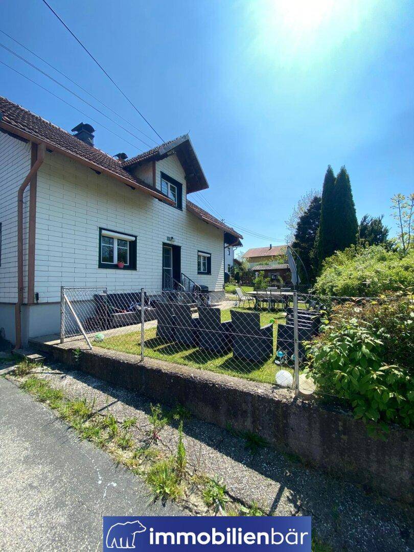 Haus mit grünem Garten und Terrasse, umzäunt, an einem sonnigen Frühlingstag.