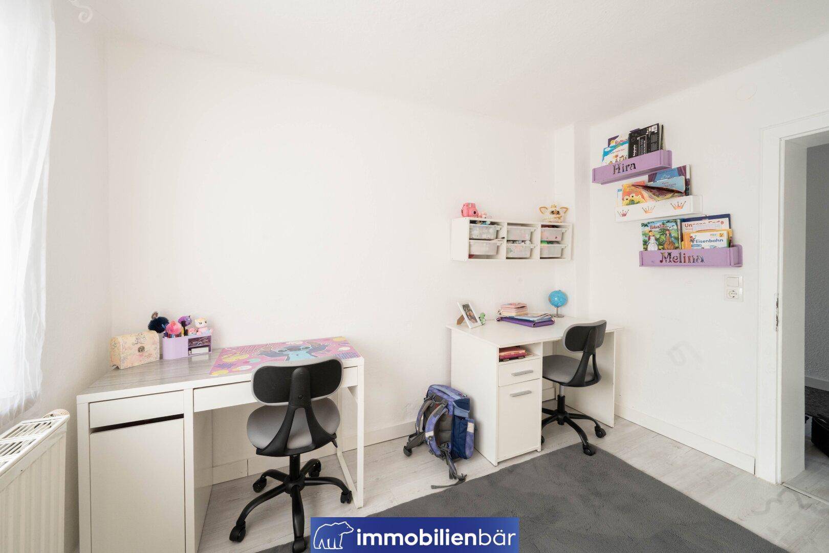 Kinderzimmer mit zwei Schreibtischen, Regalen und personalisierten Dekorationen.