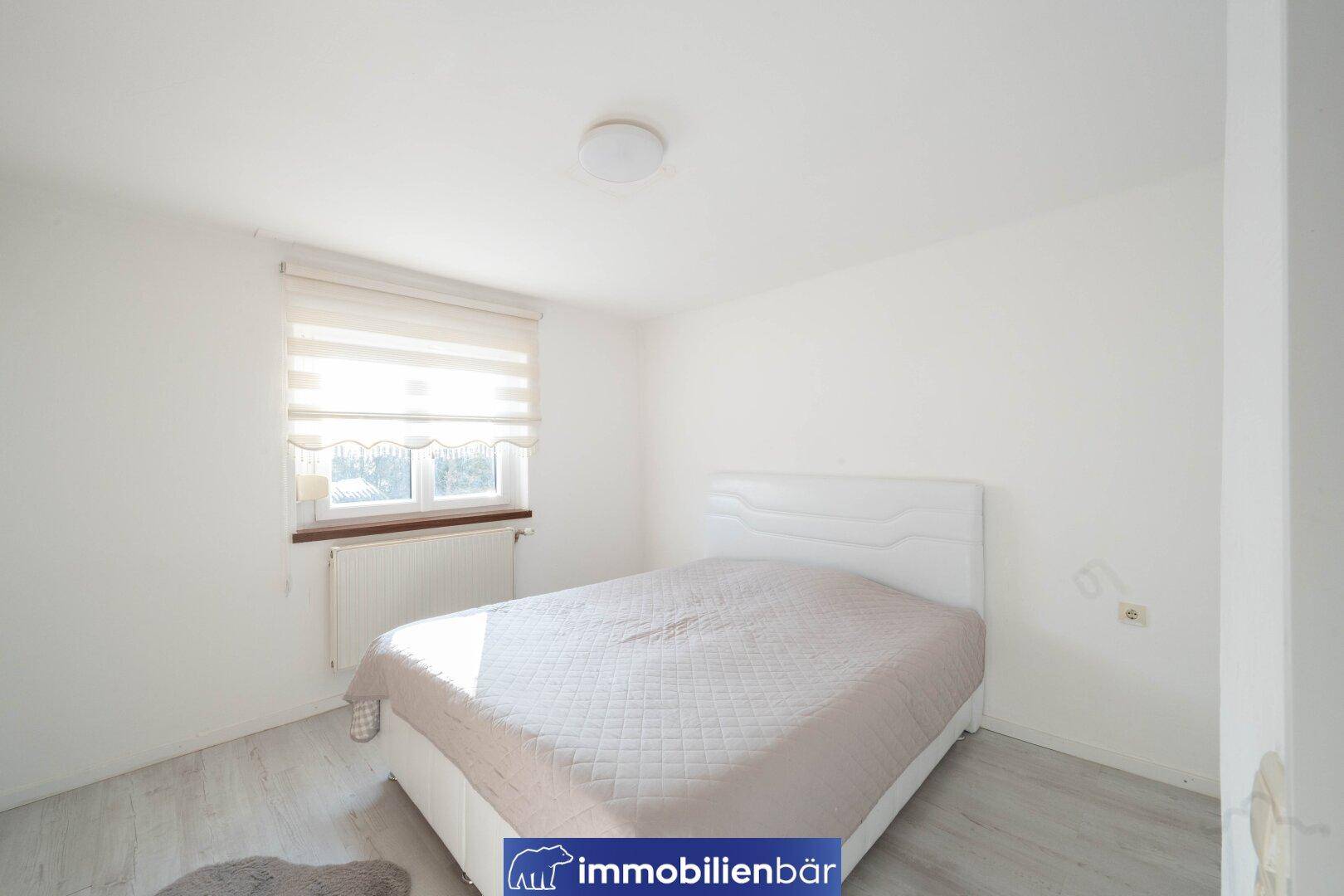 Schlafzimmer mit Doppelbett, Fenster und Heizkörper, in hellen Farben gehalten.