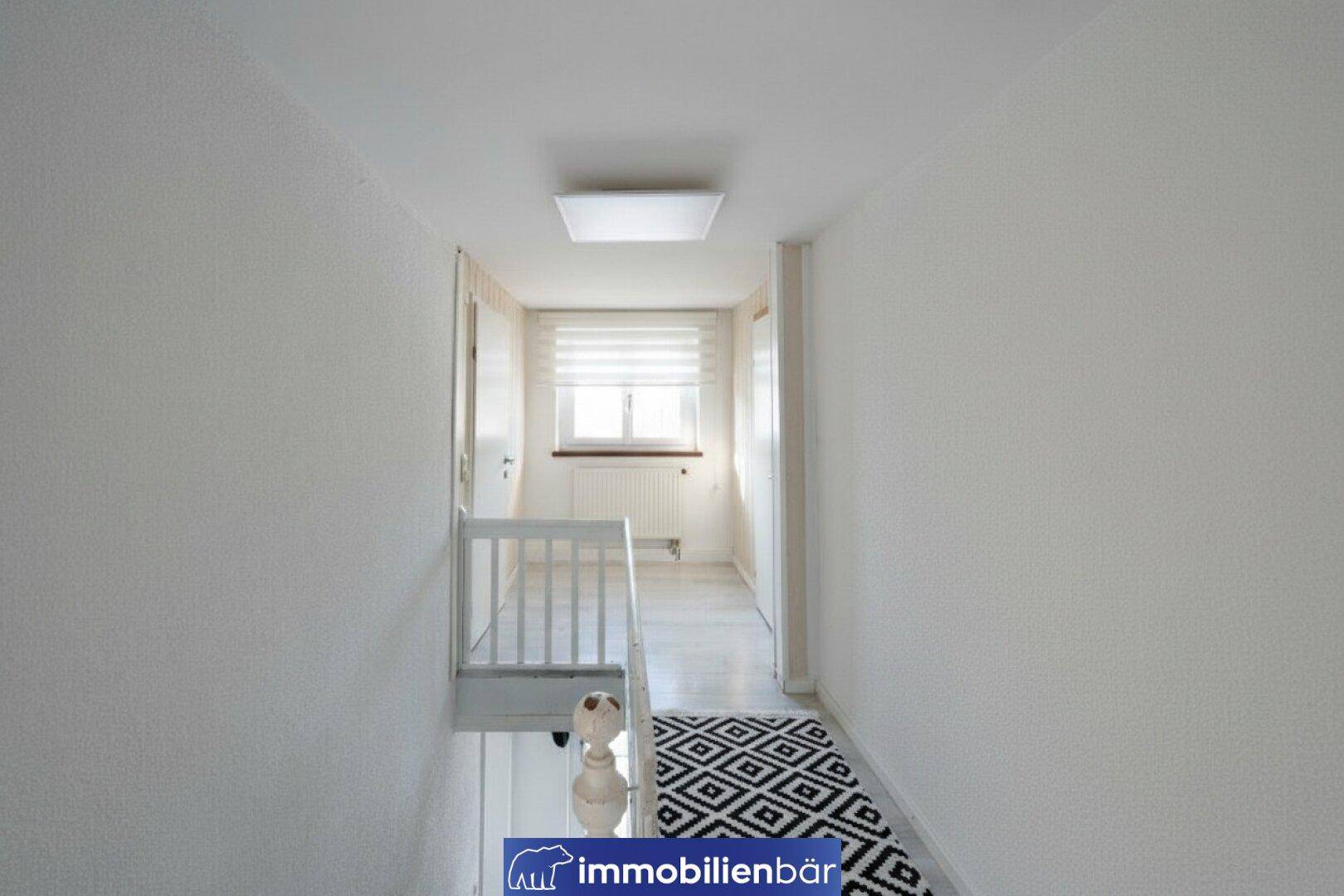 Heller Flur mit Treppenaufgang, Fenster und modernem Teppichläufer.