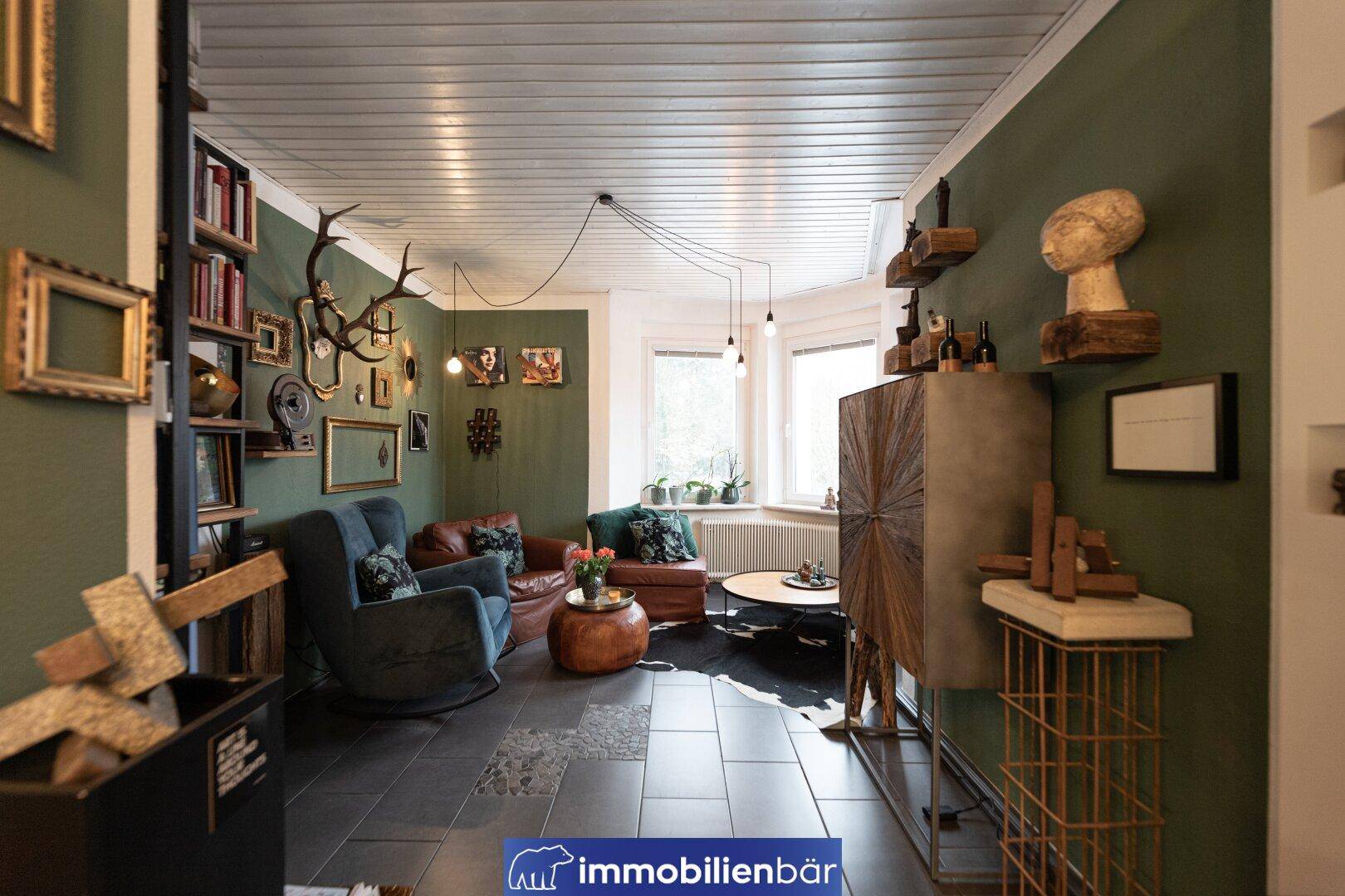 Geräumiges Wohnzimmer mit Bücherregal, bequemen Sesseln und individueller Dekoration.
